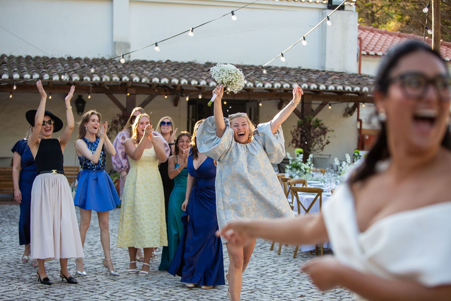 Excited wedding guests cheer as bride tosses bouquet at outdoor reception.
