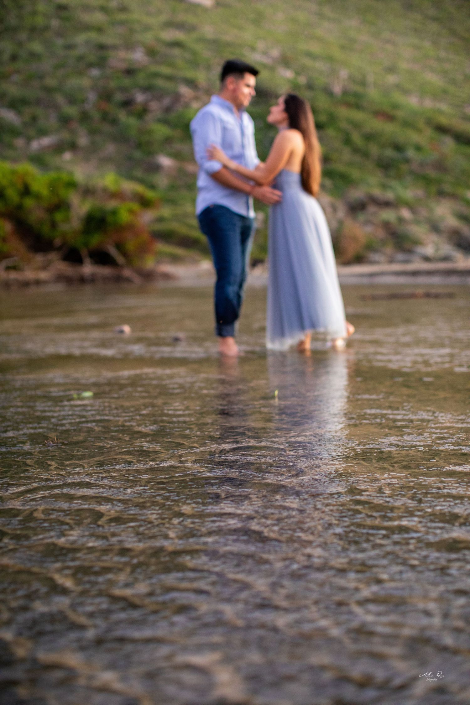 Blurred couple standing close together in shallow beach water.