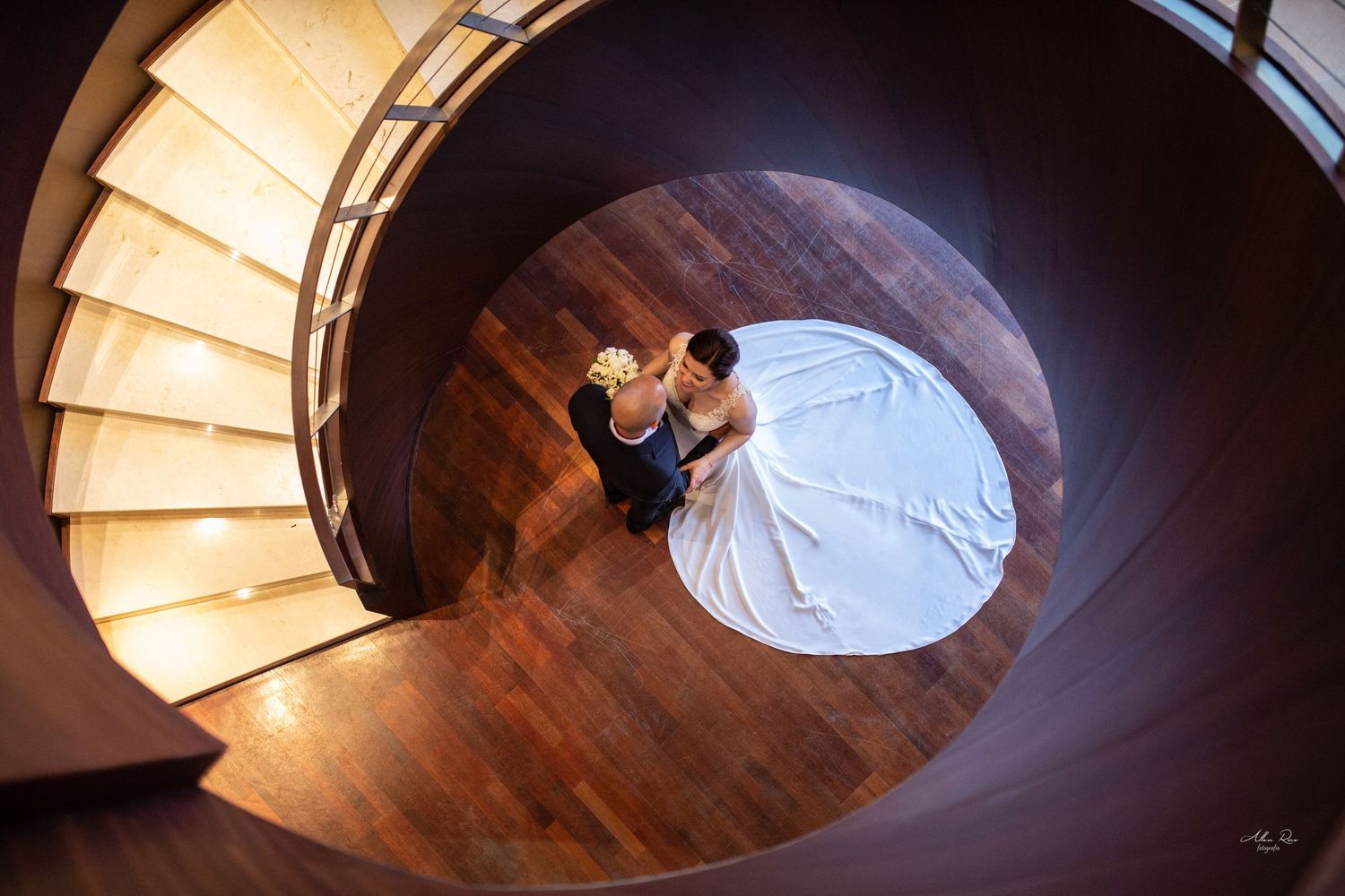 Aerial view of bride and groom dancing on a stunning circular wooden spiral staircase.