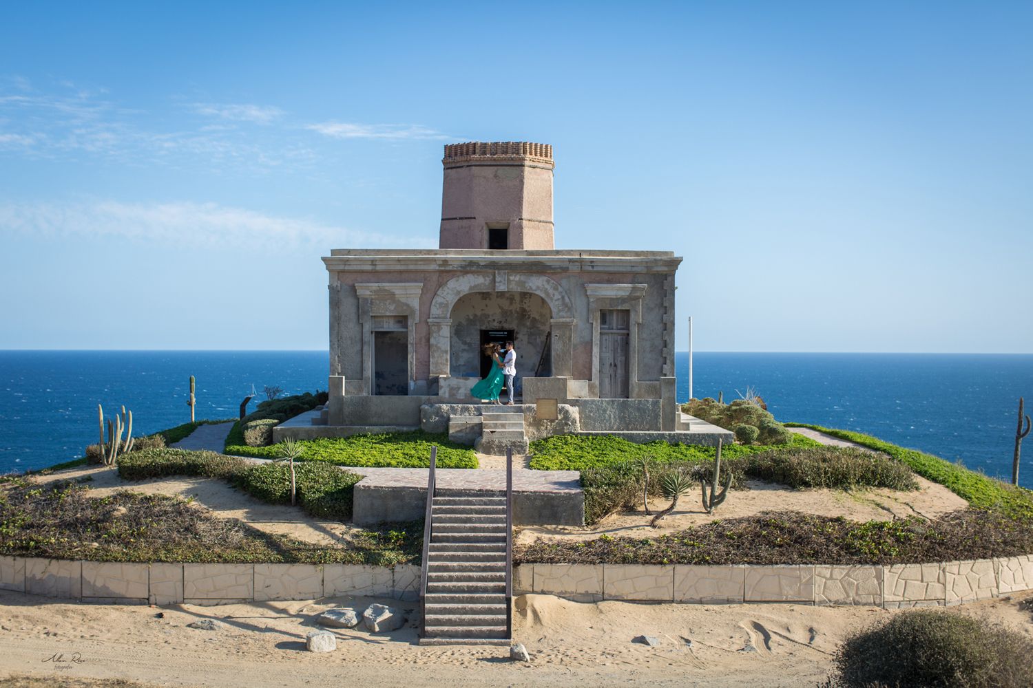 Historic stone lighthouse building with tower overlooking the blue ocean on a sunny day in Los Cabos, Mexico.