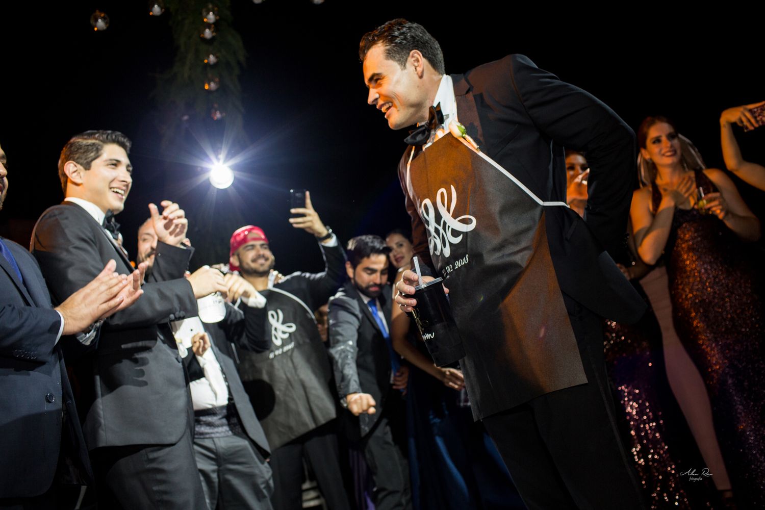 Groom being celebrated by wedding guests during outdoor evening reception.