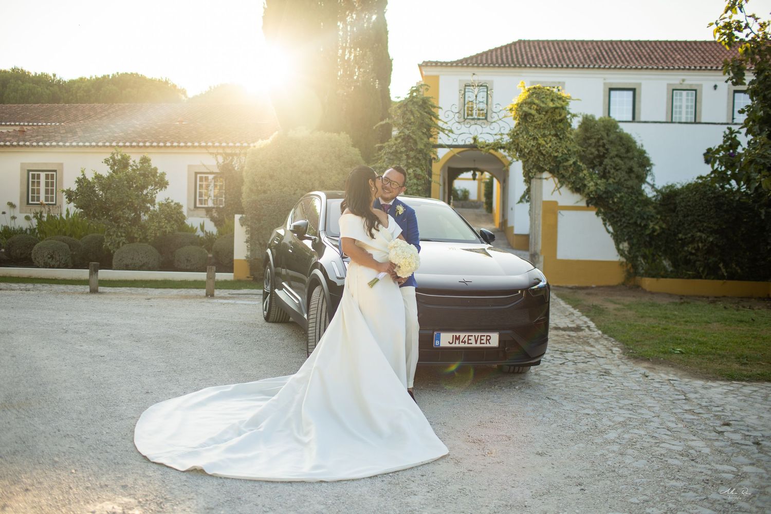 Radiant bride in white gown poses beside luxury SUV at golden sunset.