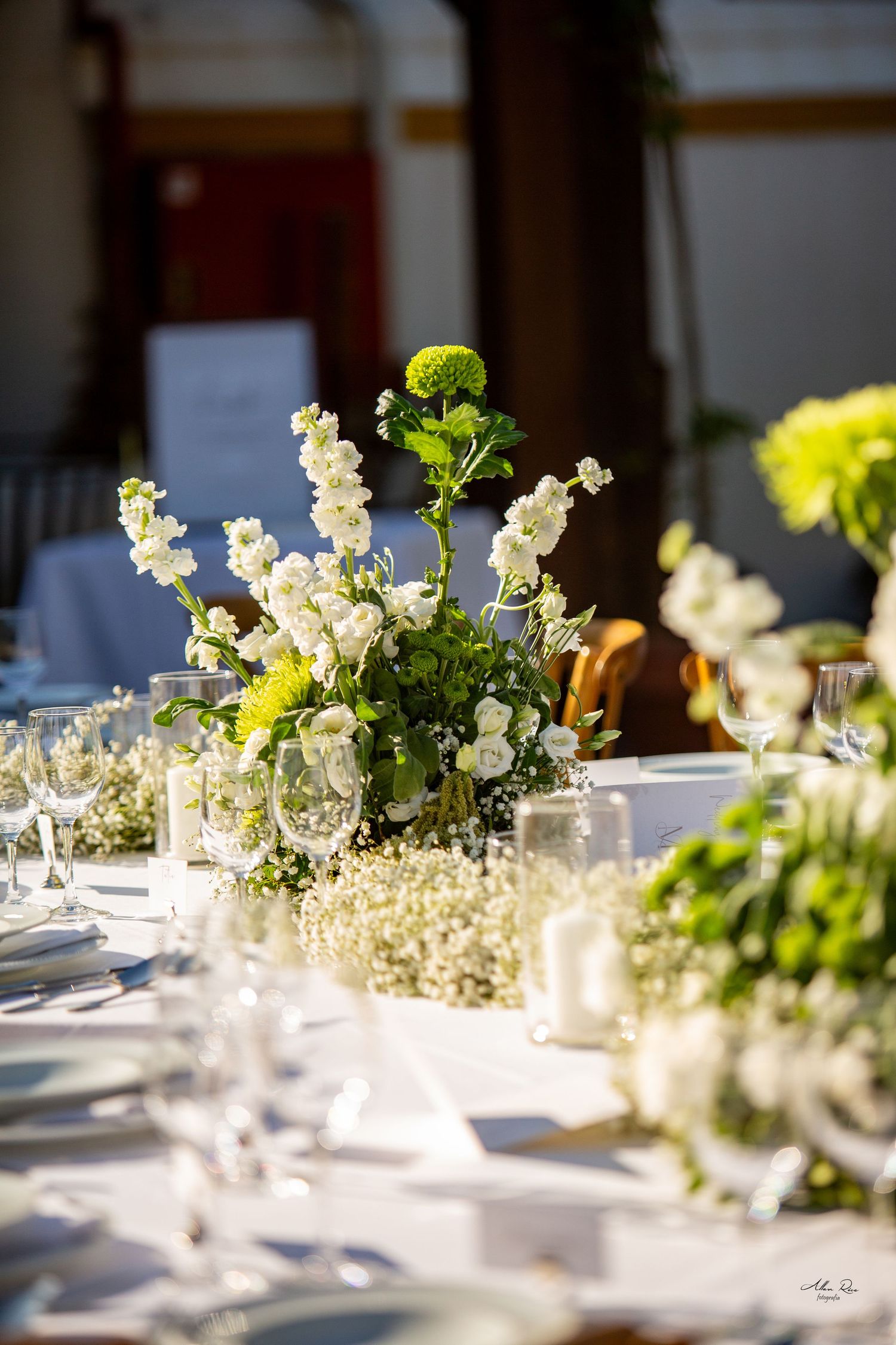Elegant wedding reception table with white and green floral centerpieces and crystal glassware.