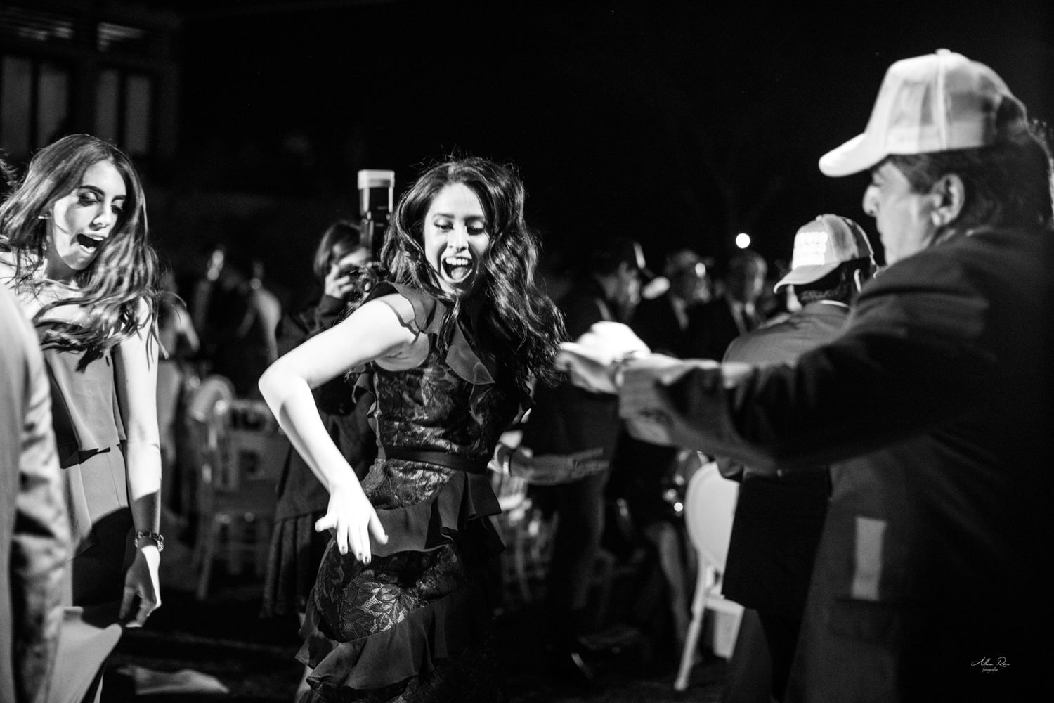 Black and white photo of woman dancing energetically with guests at lively outdoor wedding reception.