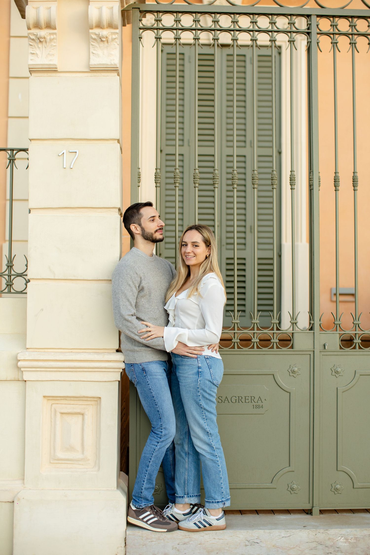 Young couple embracing by an ornate green gate at building number 17 in a European city.