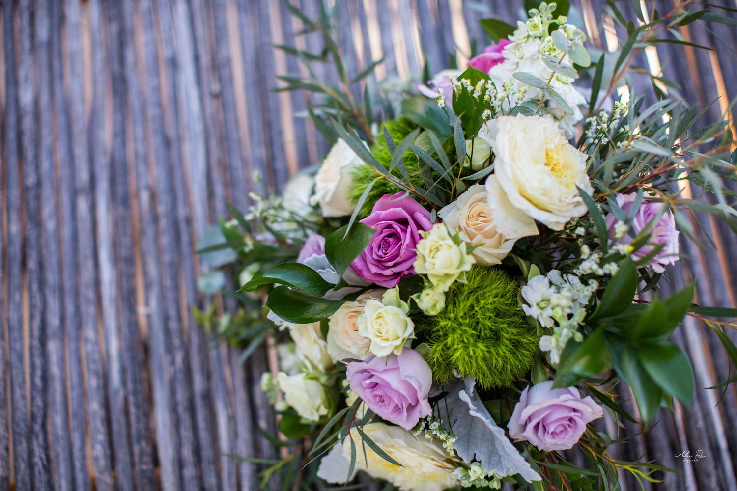Romantic bridal bouquet with pink, purple, and cream roses with greenery on a rustic wooden background.