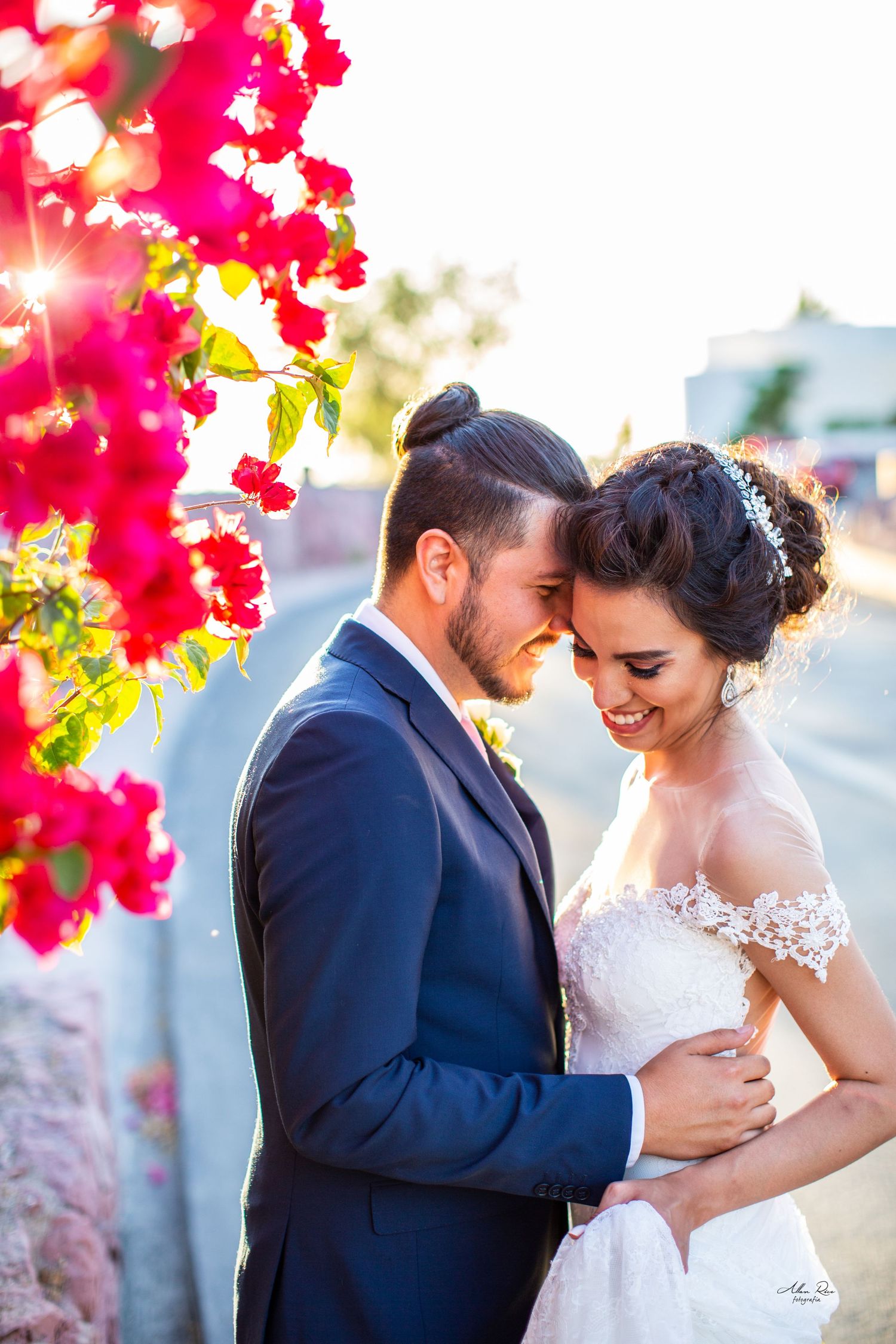 Bride and groom embrace tenderly near vibrant pink bougainvillea flowers in warm golden sunset light.