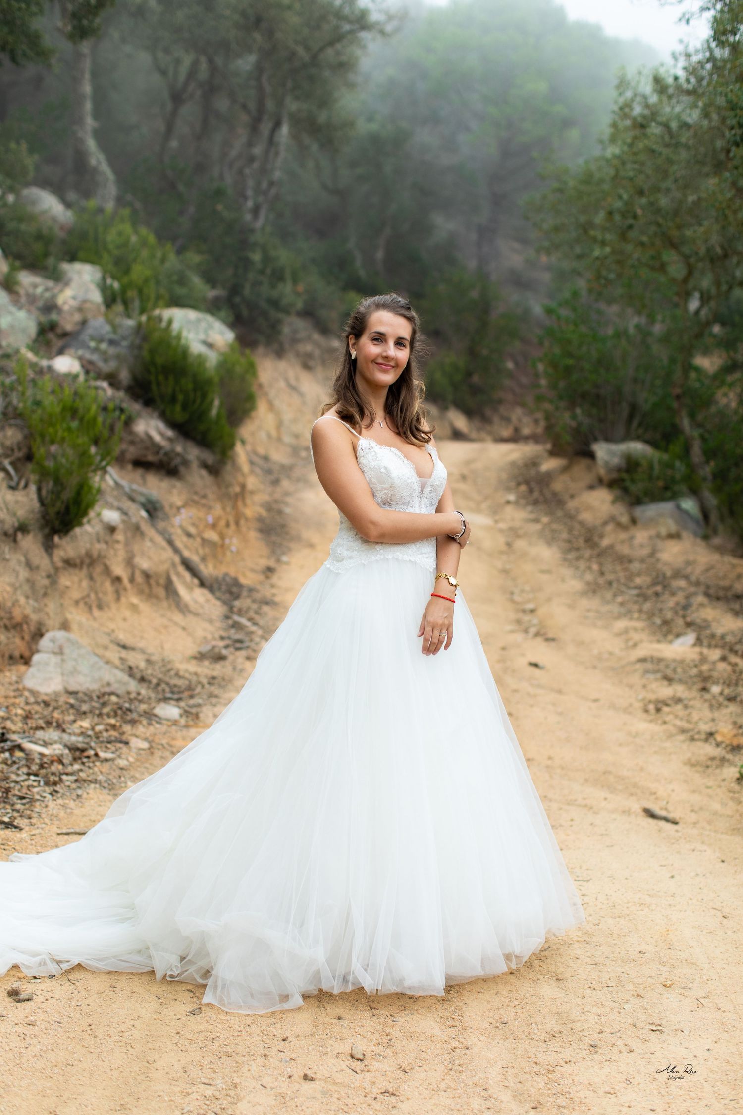 Radiant bride in flowing white tulle ball gown poses on scenic dirt path.