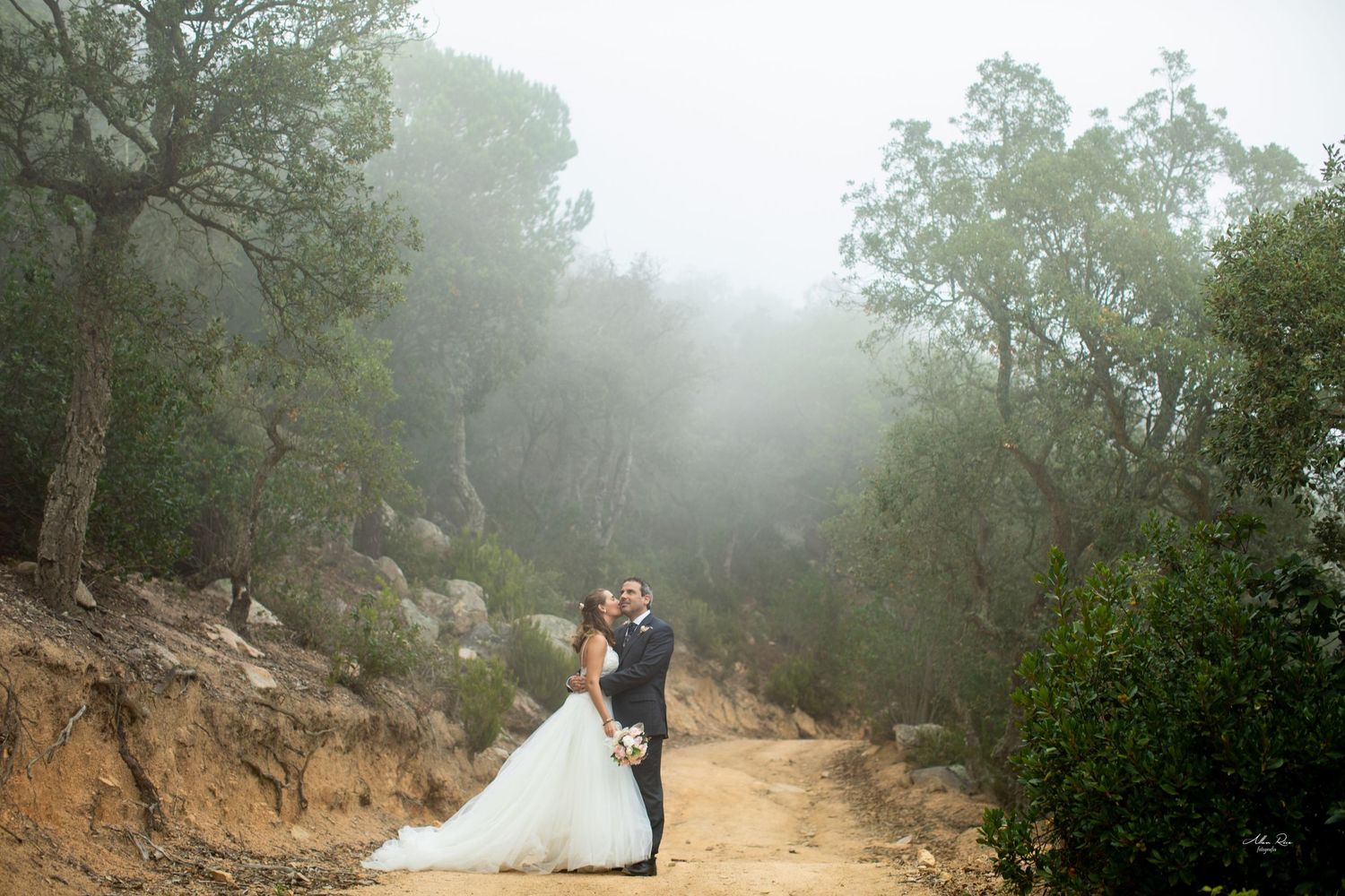 Bride and groom embrace on a misty forest trail in romantic outdoor wedding portrait.