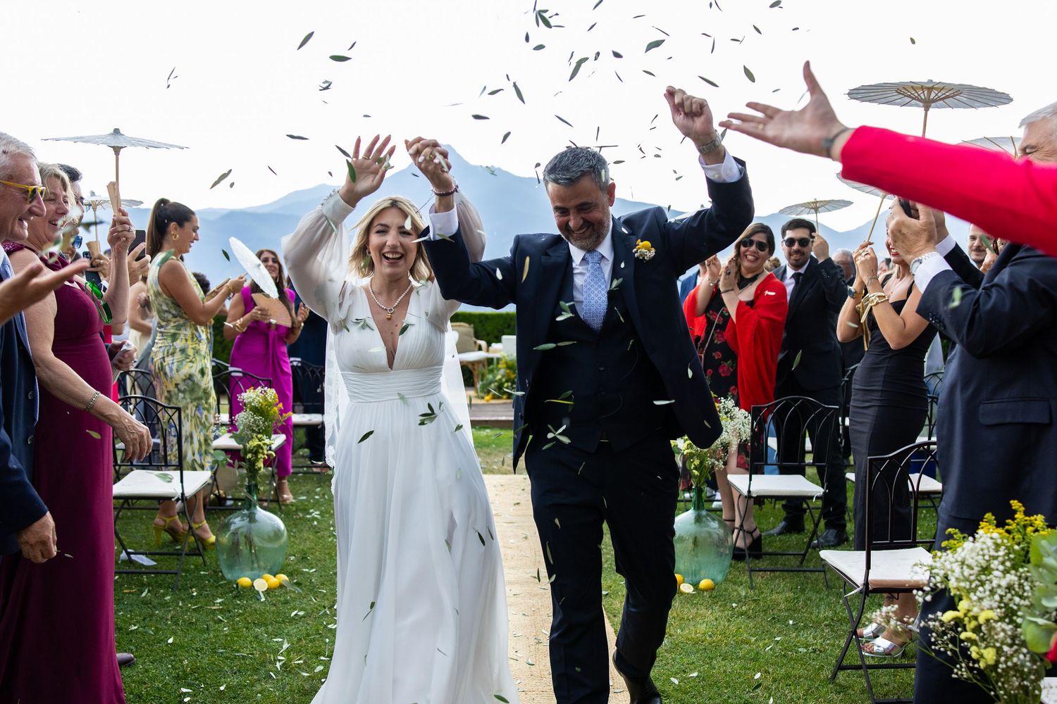 Newlyweds walk down aisle as guests toss confetti at outdoor mountain wedding.