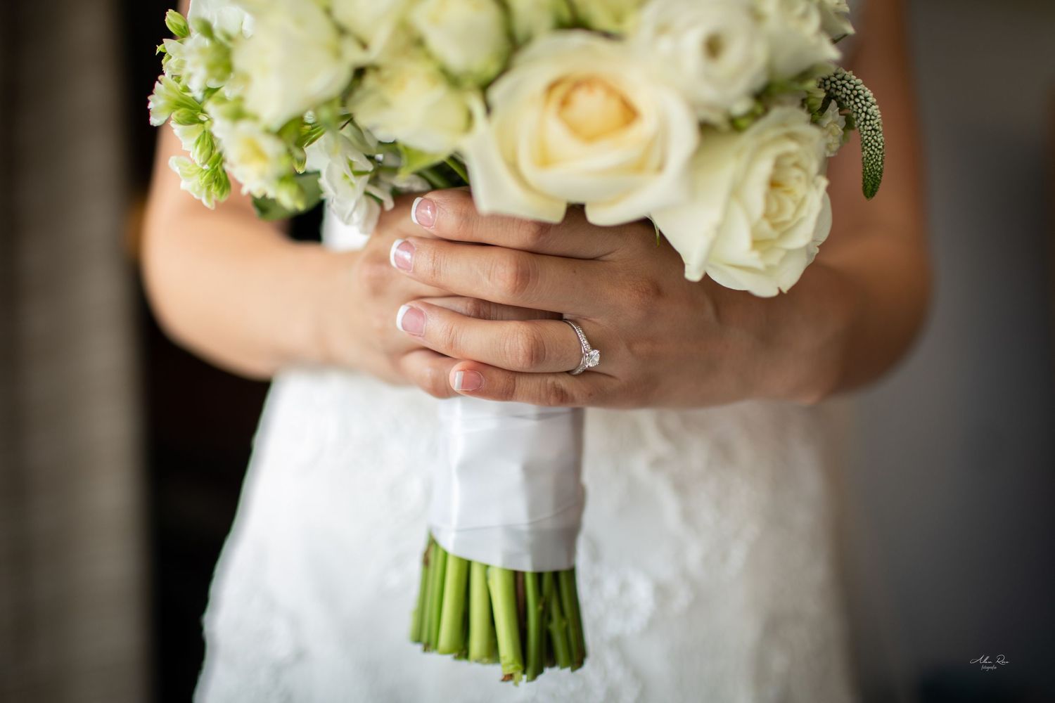Bride holds elegant white rose bouquet showing diamond engagement ring on wedding day.