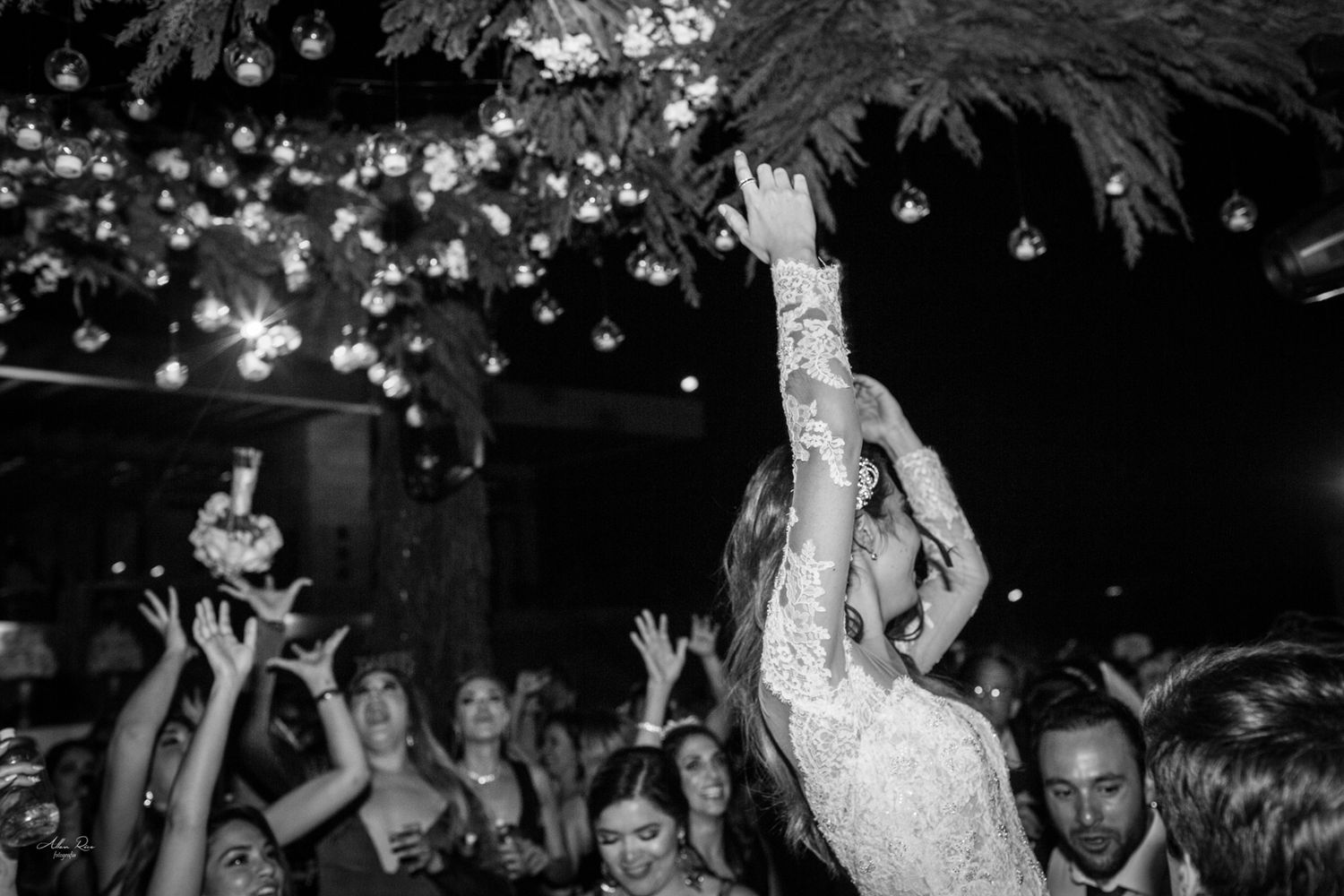 Bride tossing bouquet to excited guests at night wedding celebration.