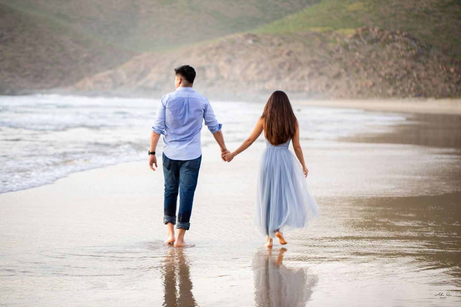 Couple walking hand in hand along scenic beach shoreline.