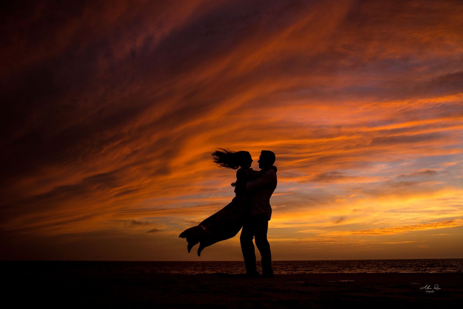 Romantic couple silhouetted against a stunning fiery sunset sky on the beach.