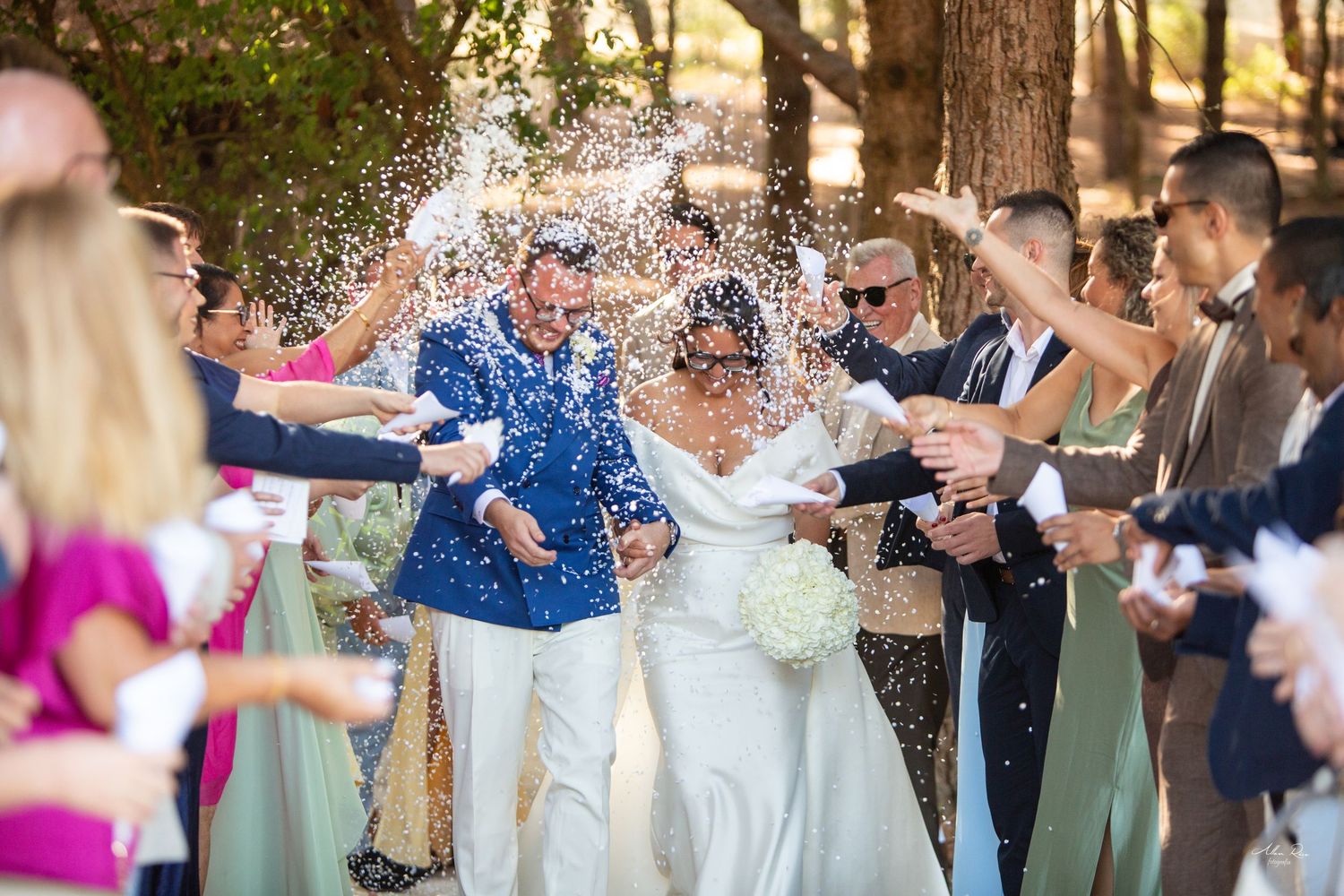 Bride and groom showered with confetti by cheering guests during outdoor wedding celebration.