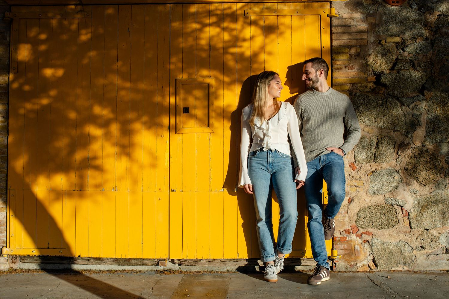 Happy couple holding hands in front of a vibrant yellow wooden door outdoors.