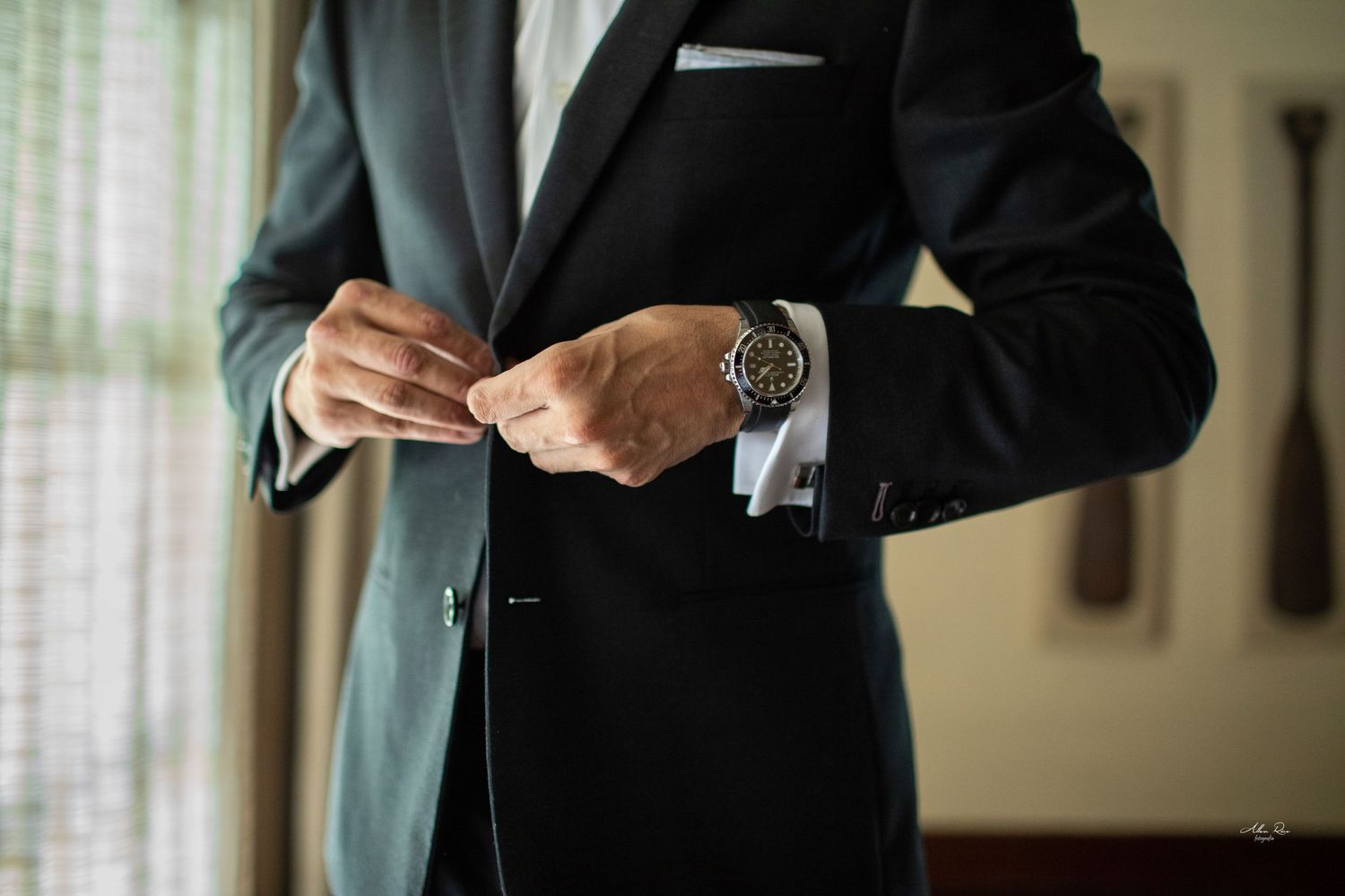 Groom in dark suit adjusts jacket button revealing luxury watch and white French cuff shirt.
