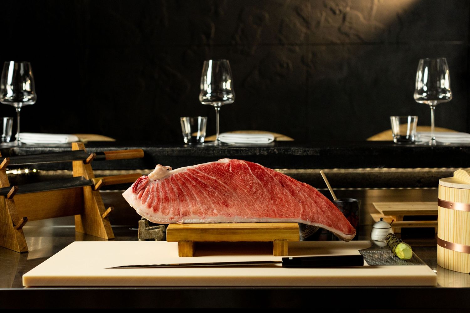 Large raw tuna block displayed on wooden cutting board in upscale Japanese restaurant with elegant table settings.