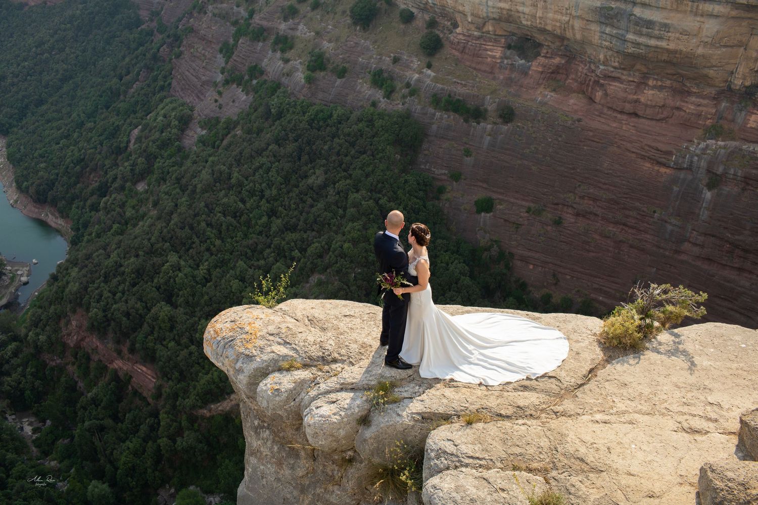 Wedding couple poses on dramatic canyon cliff edge with sweeping valley views below.