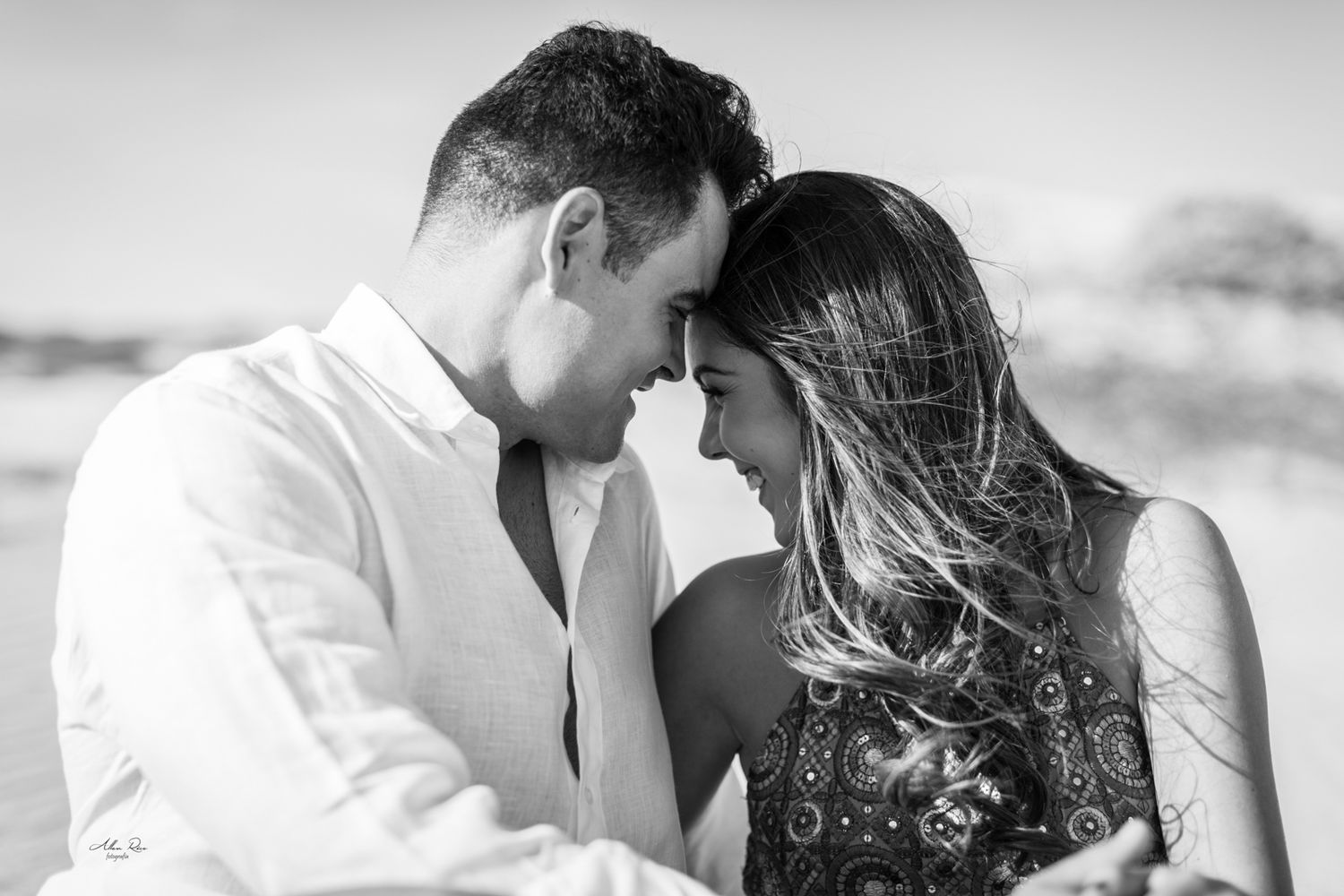 Black and white close-up of a romantic couple touching foreheads tenderly on the beach.