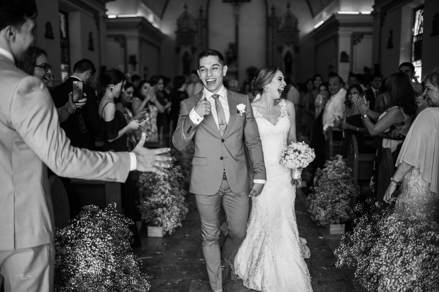 Newlyweds walk joyfully down church aisle surrounded by cheering guests after wedding ceremony.
