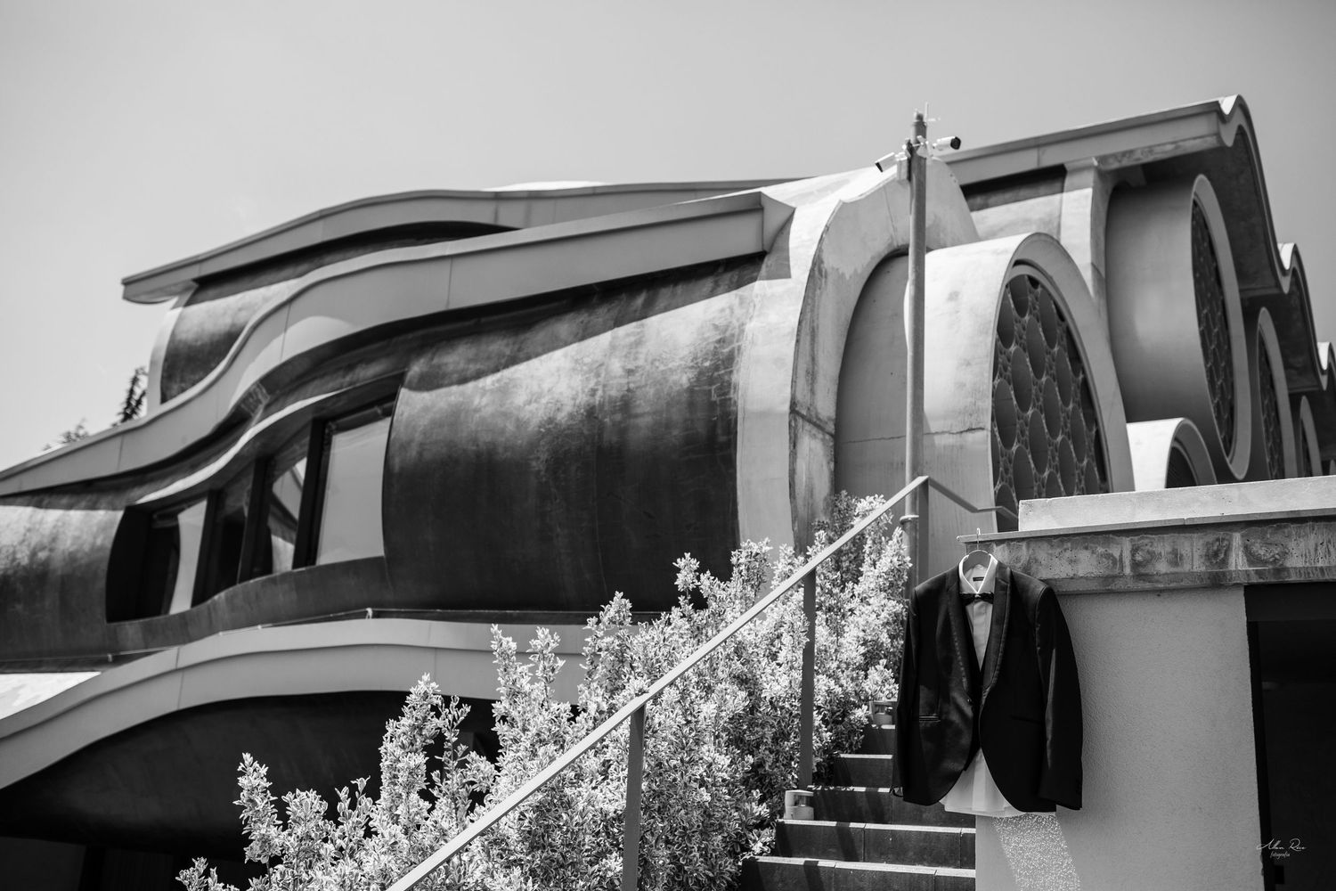 Black and white exterior shot of a modern church with groom's suit on railing.