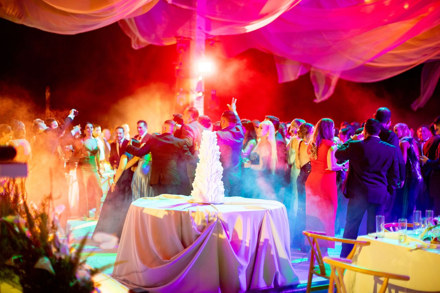 Colorful wedding cake cutting ceremony with dramatic smoke effects and vibrant red and yellow lighting.