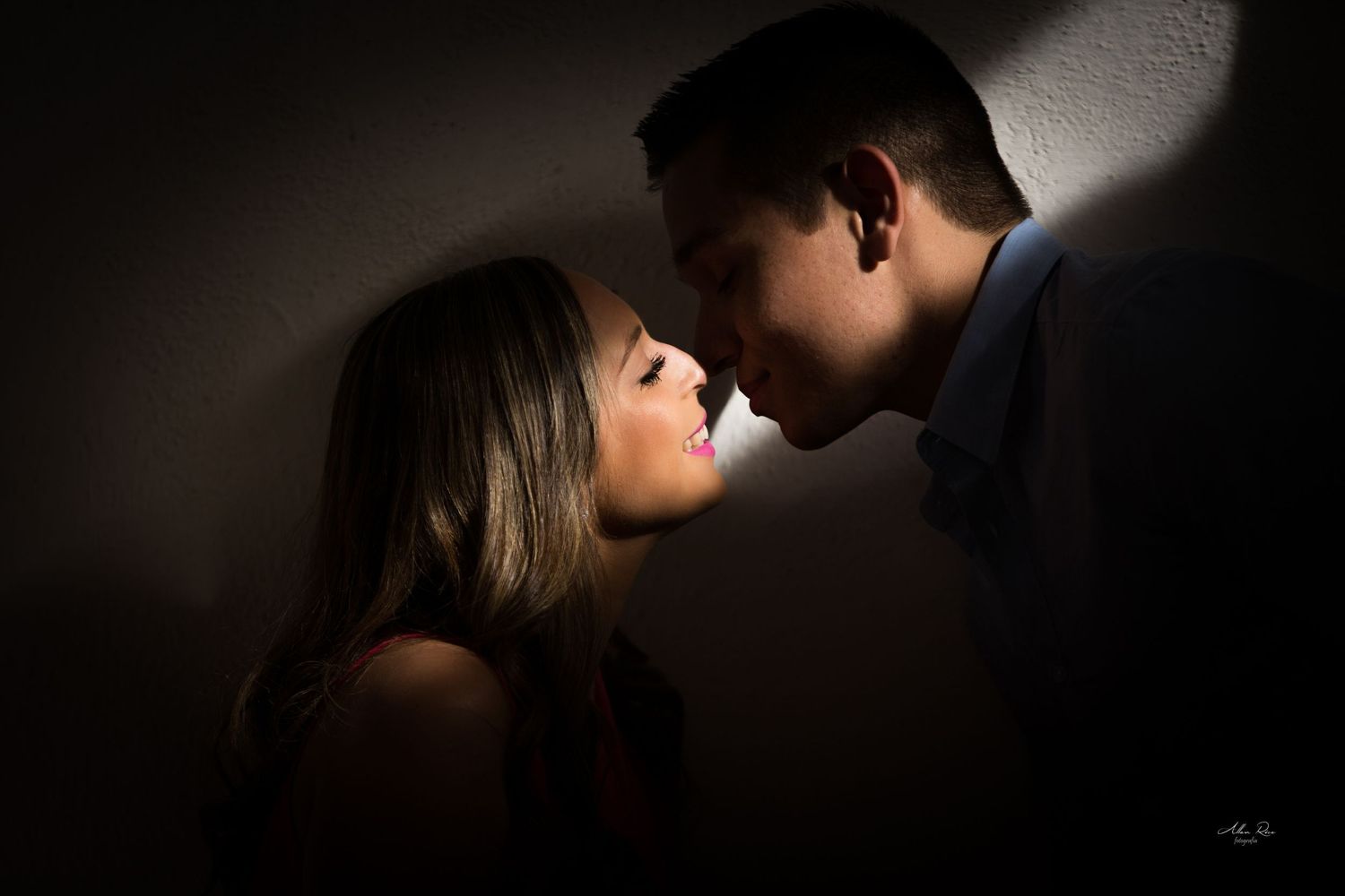 Romantic couple nearly kissing in dramatic shadow lighting during an intimate engagement portrait.