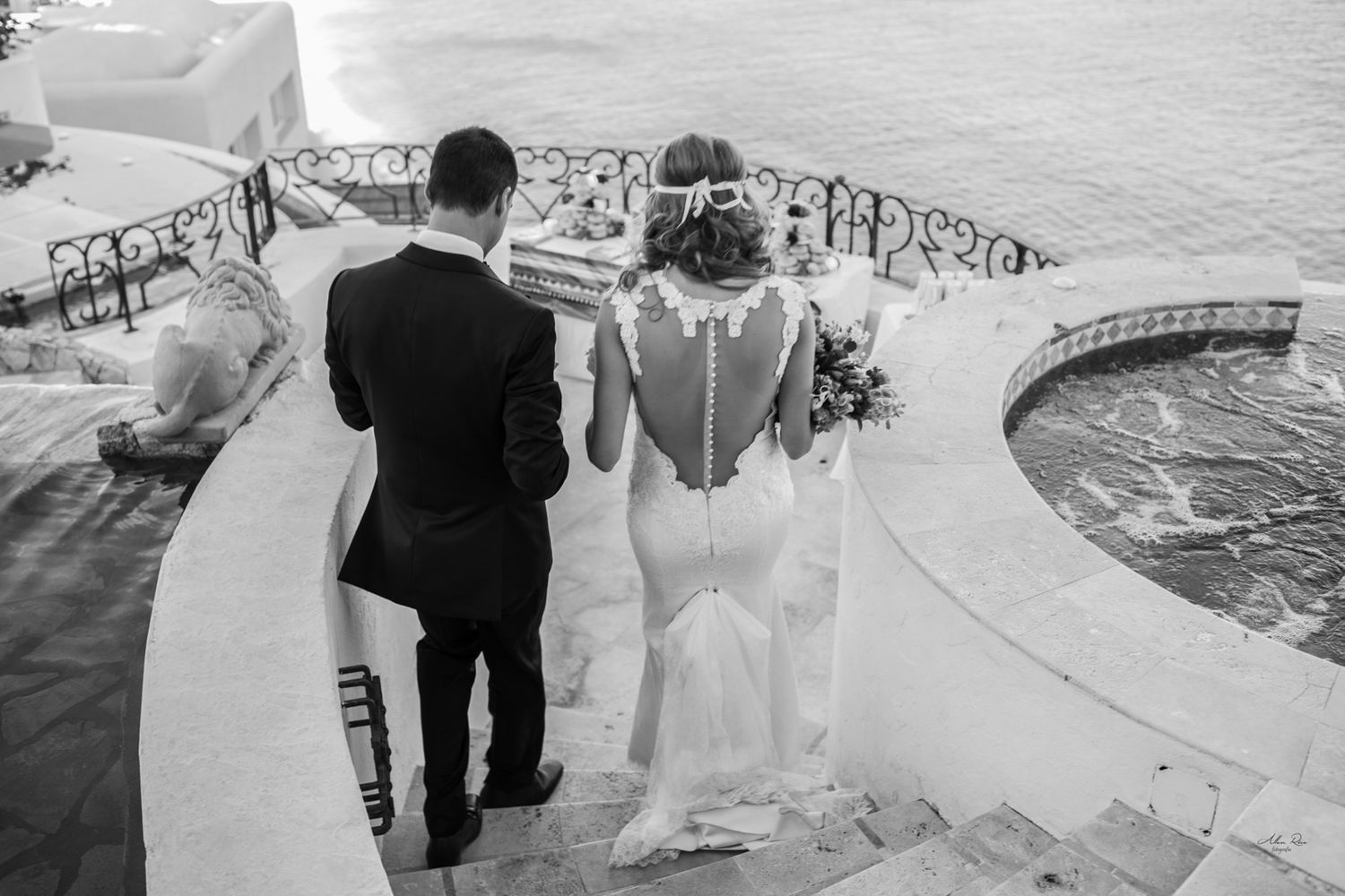 Black and white photo of bride and groom walking toward ocean view terrace.