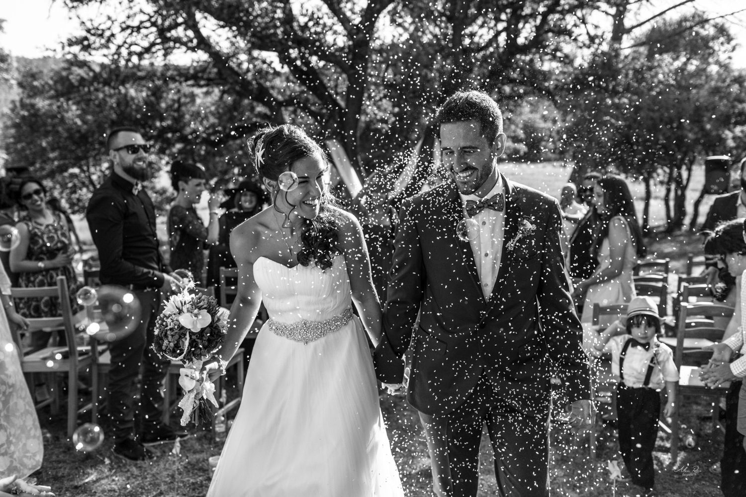A bride and groom walk joyfully through a shower of confetti at their outdoor wedding reception.