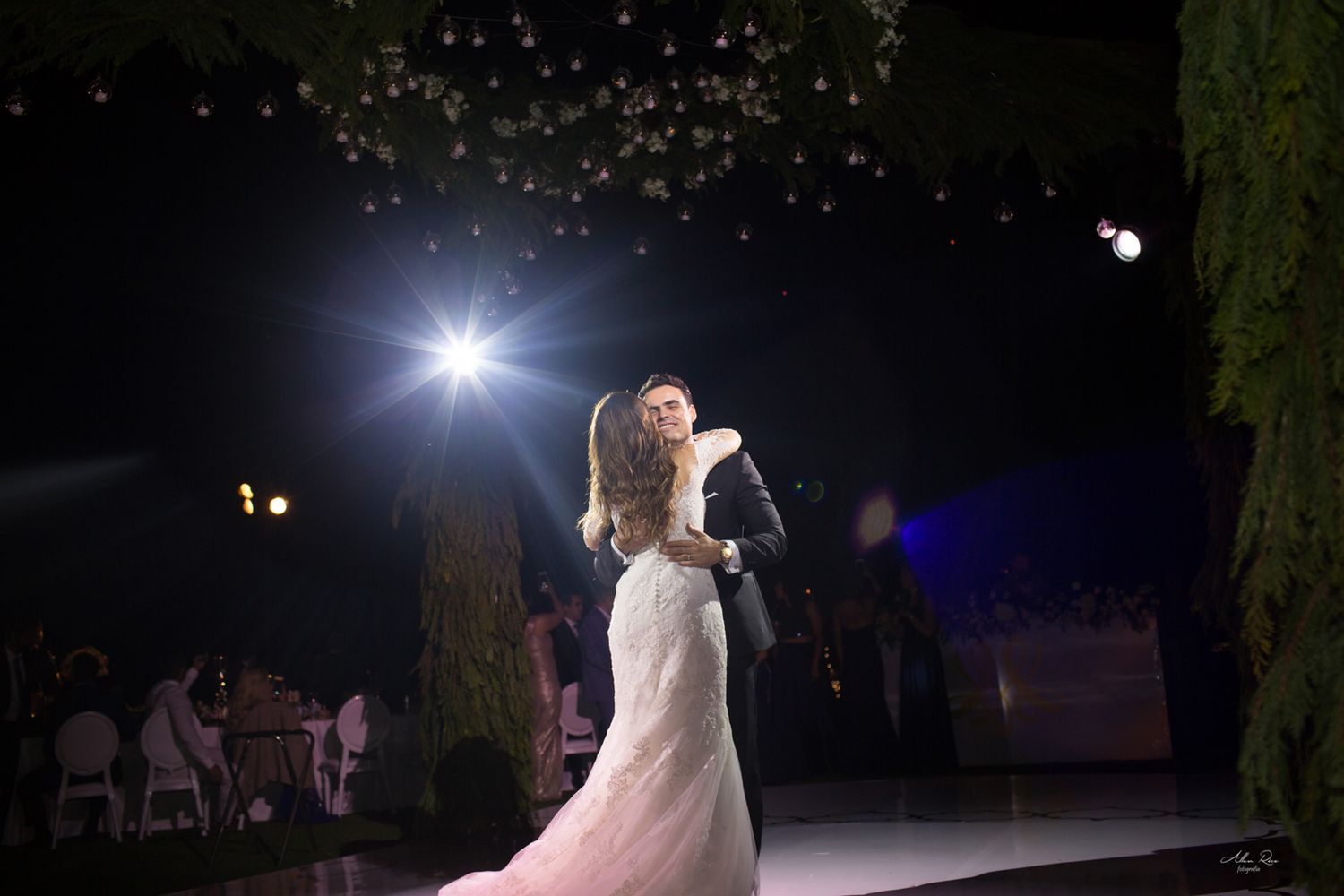 Bride and groom dancing under sparkling lights at romantic outdoor night wedding.