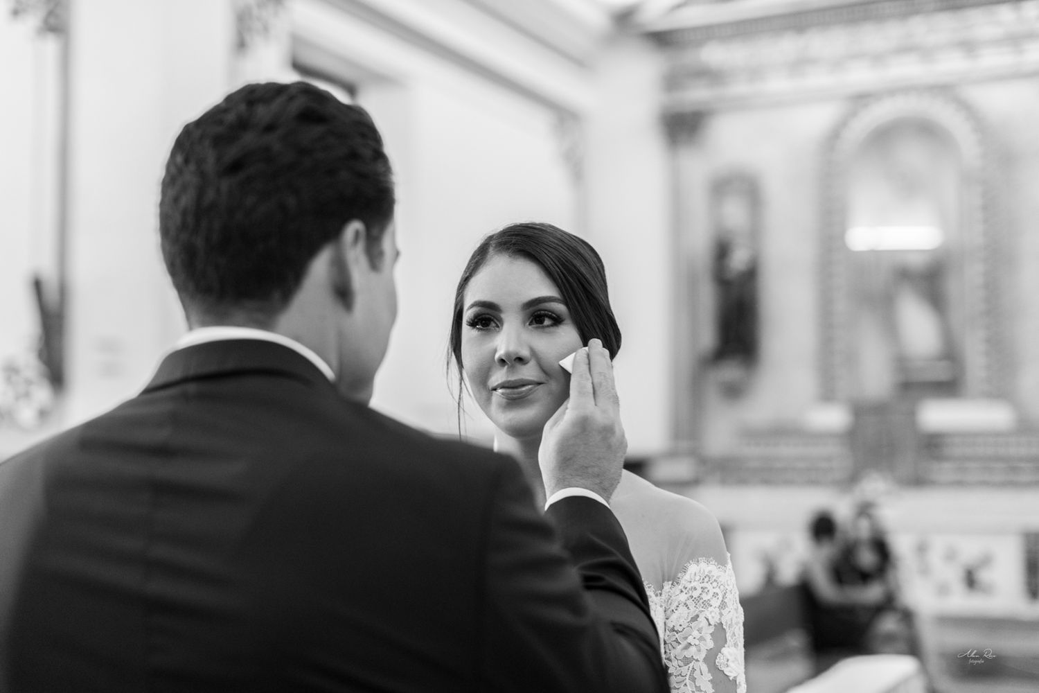 Groom gently wipes tears from bride's cheek during emotional wedding ceremony in church.