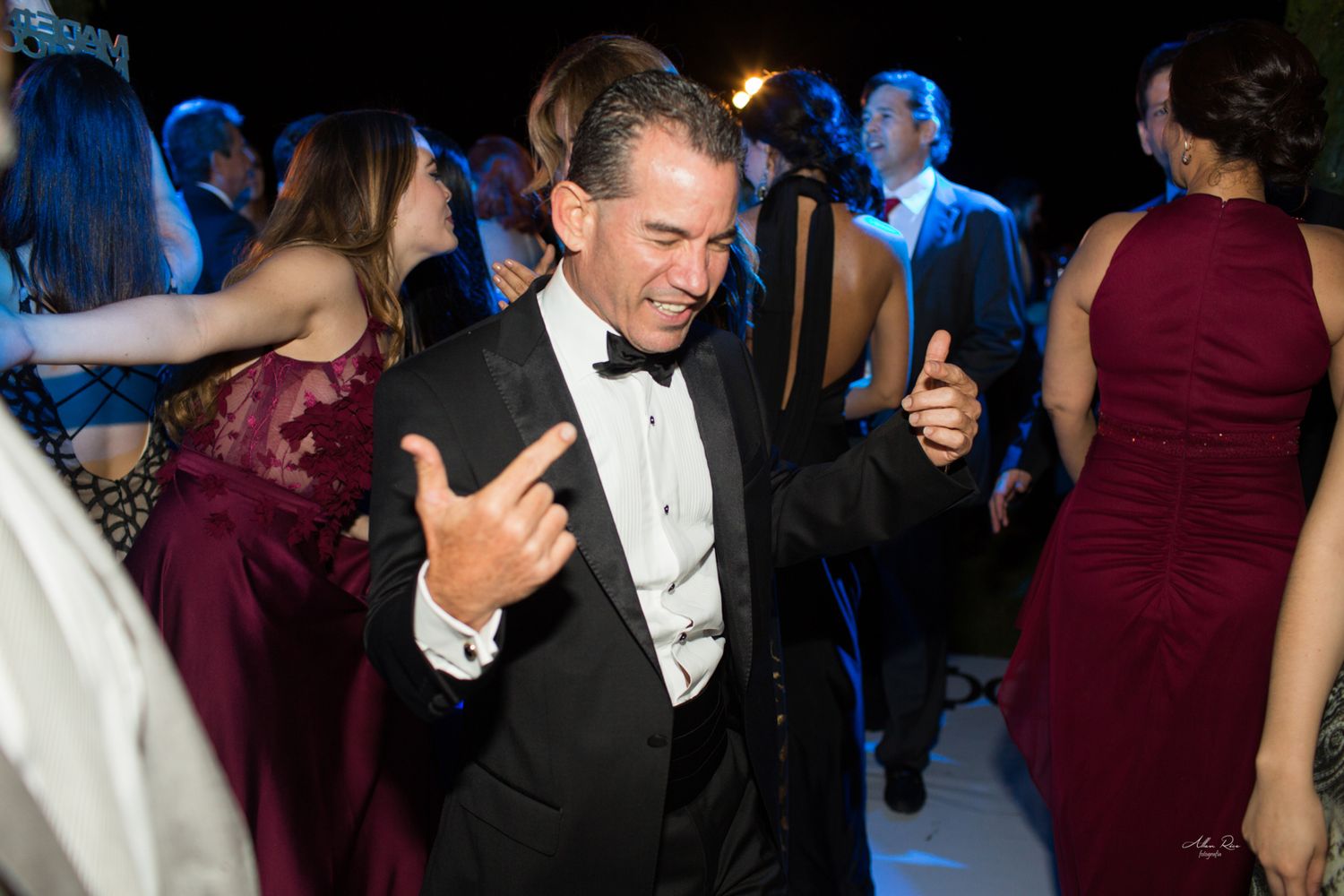 Man in tuxedo dancing enthusiastically at a wedding reception party.