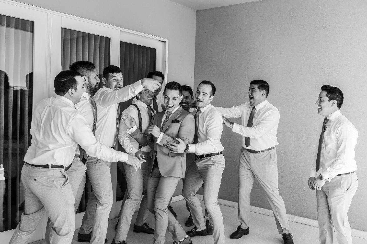 Groomsmen playfully celebrating together in a room during wedding preparations in a black and white photo.