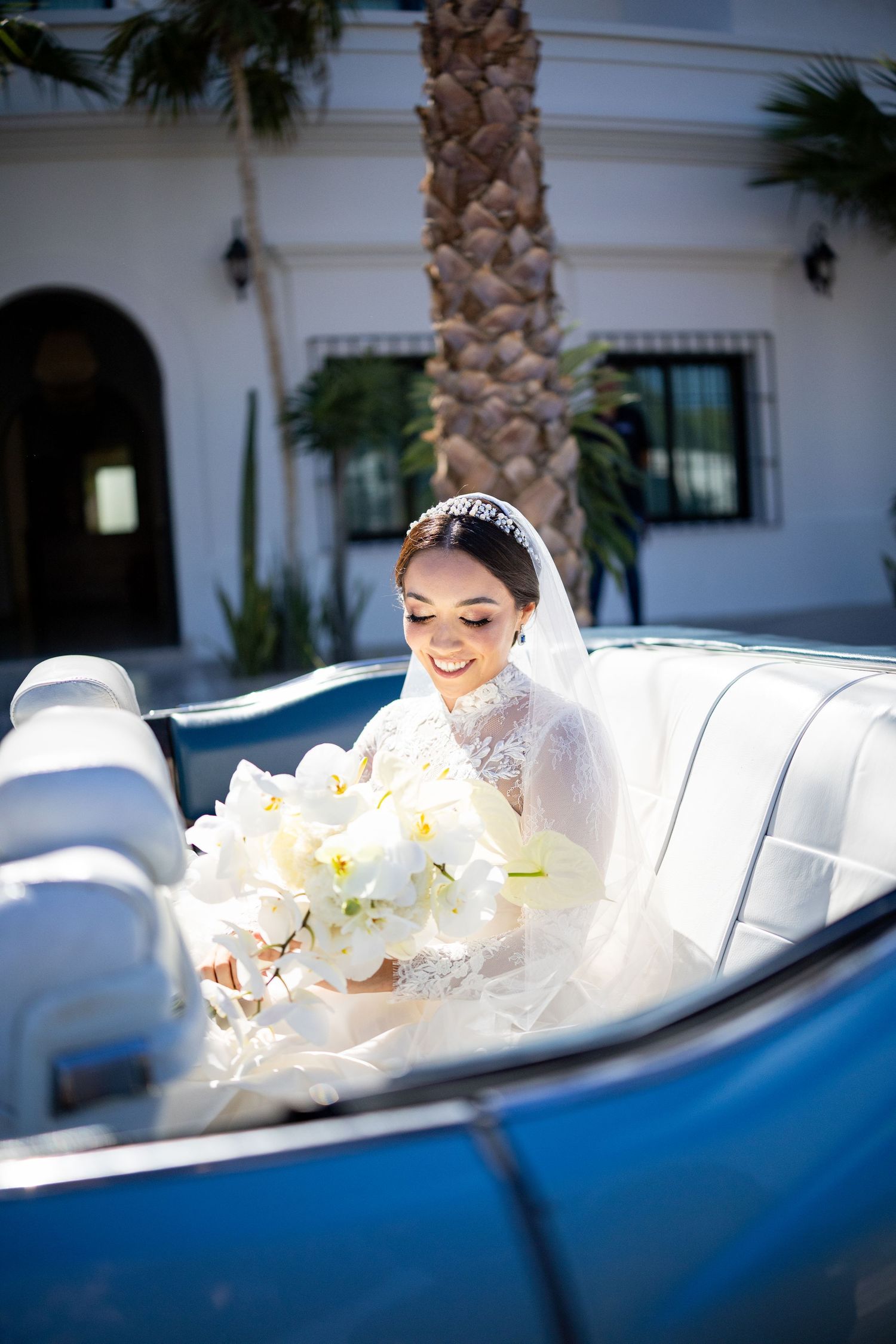 Radiant bride holding white orchid bouquet while seated in a vintage blue convertible.