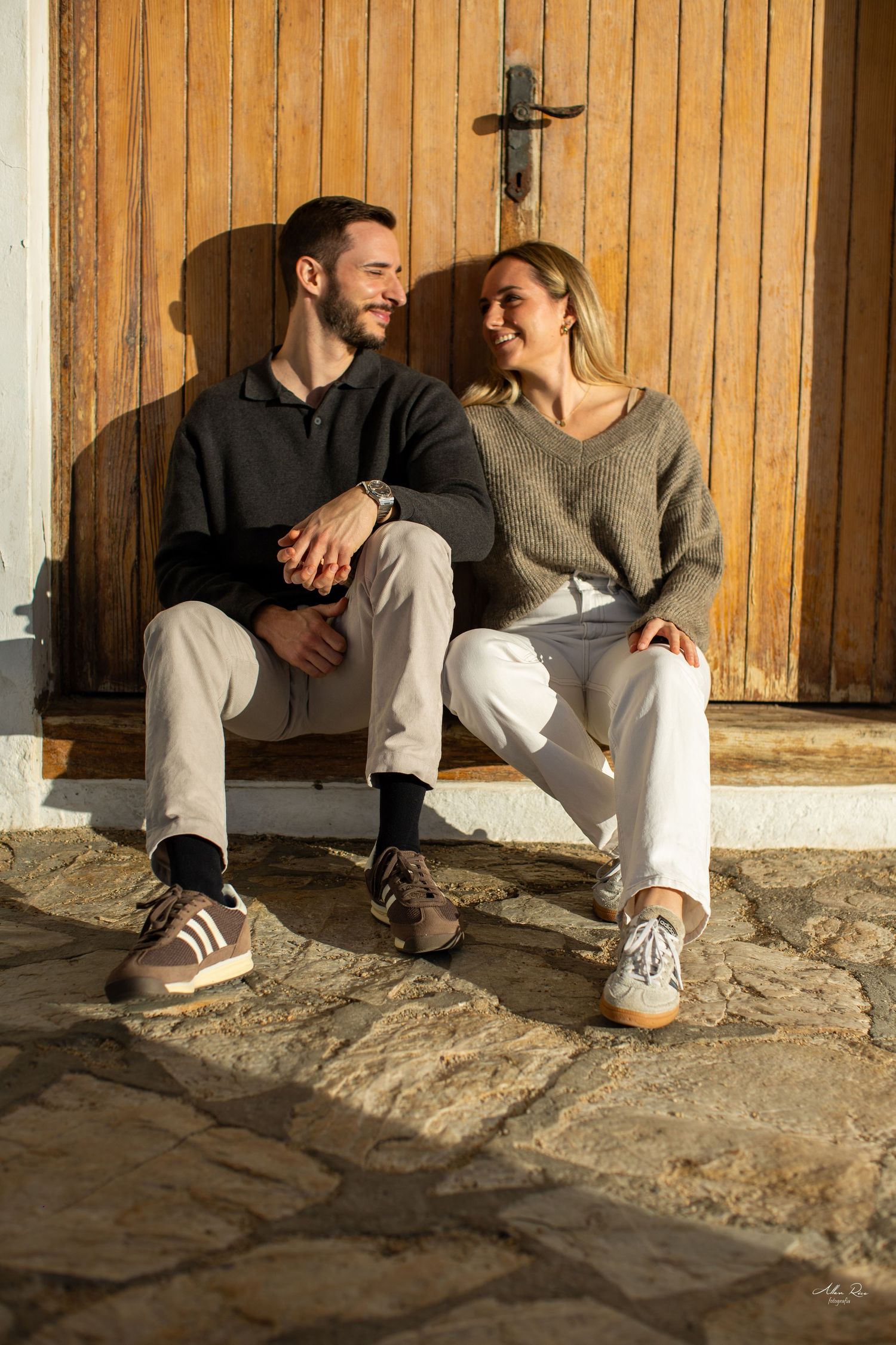 Happy couple sitting together on stone steps against rustic wooden door in warm golden sunlight.
