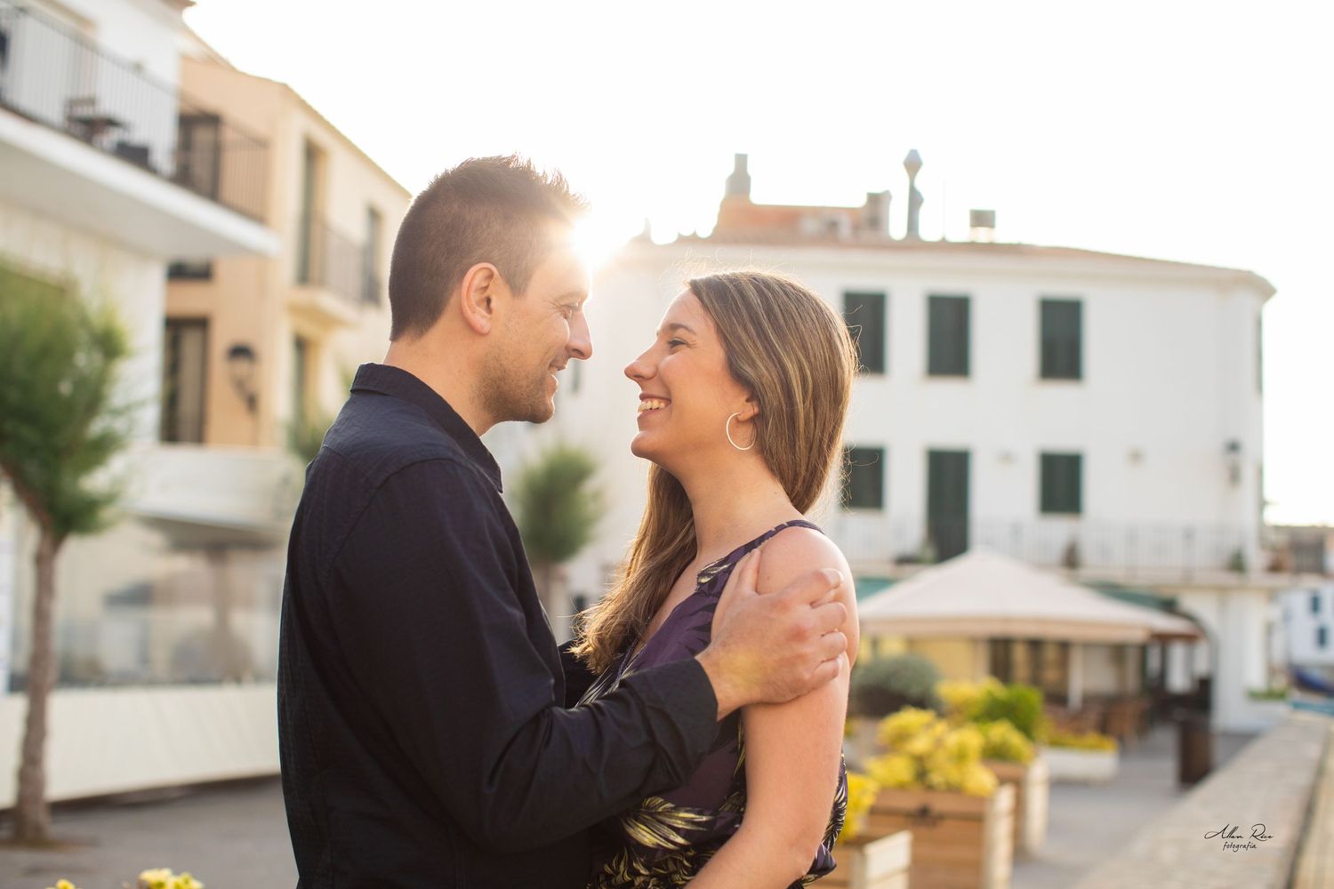 Happy couple sharing a joyful embrace in a sunlit European town square setting.