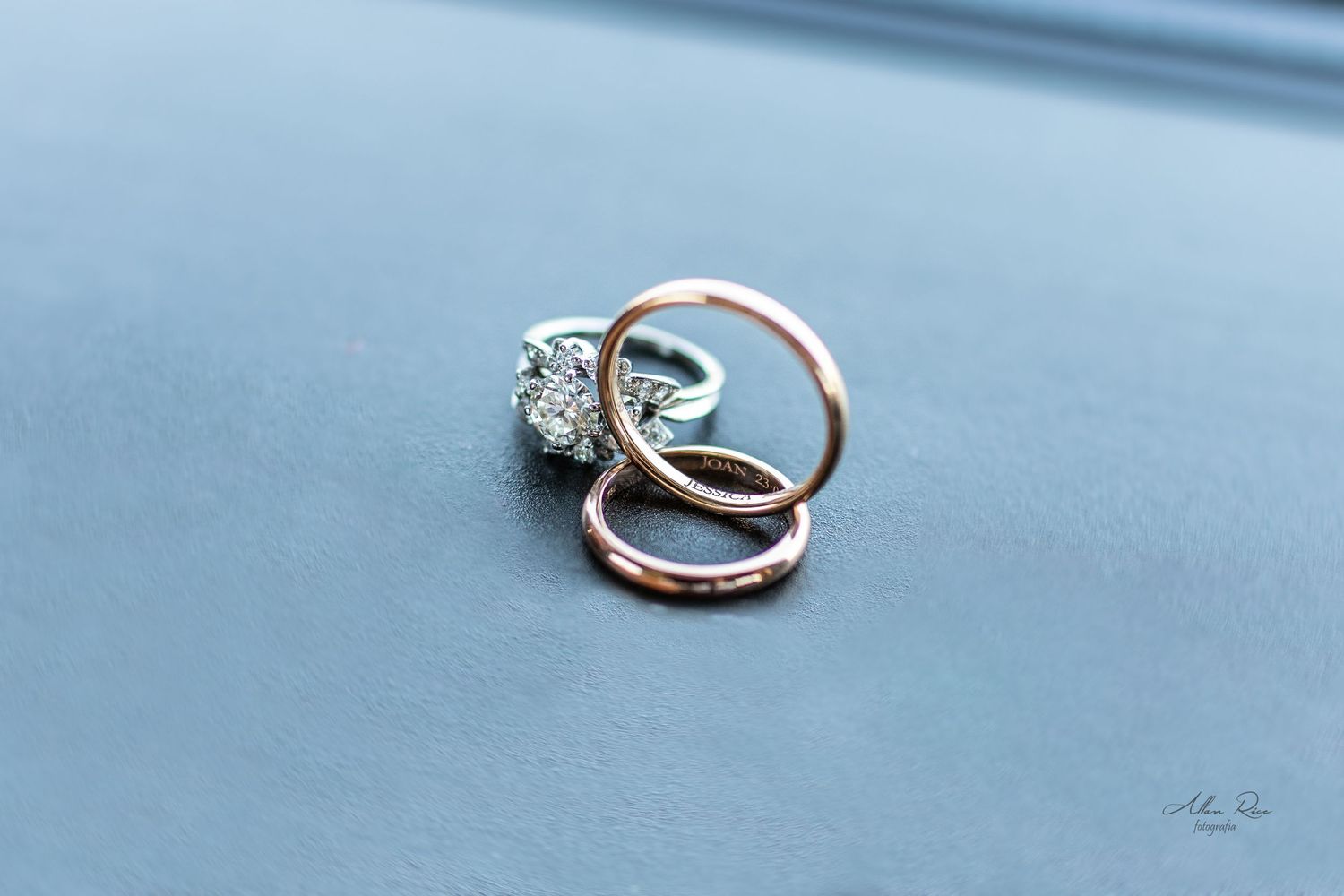 Diamond engagement ring with two rose gold wedding bands resting on light blue surface.