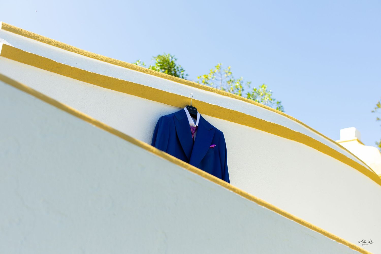 Blue wedding suit jacket displayed on yellow and white striped wall outdoors.