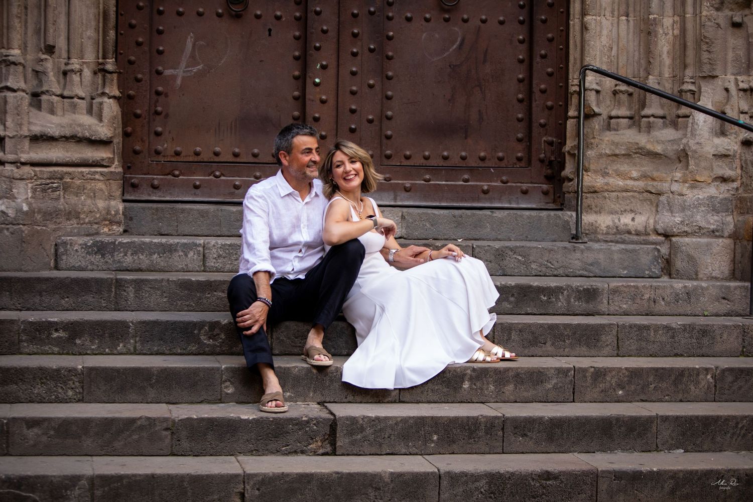 Happy couple sitting together on stone steps in front of a grand historic wooden door.