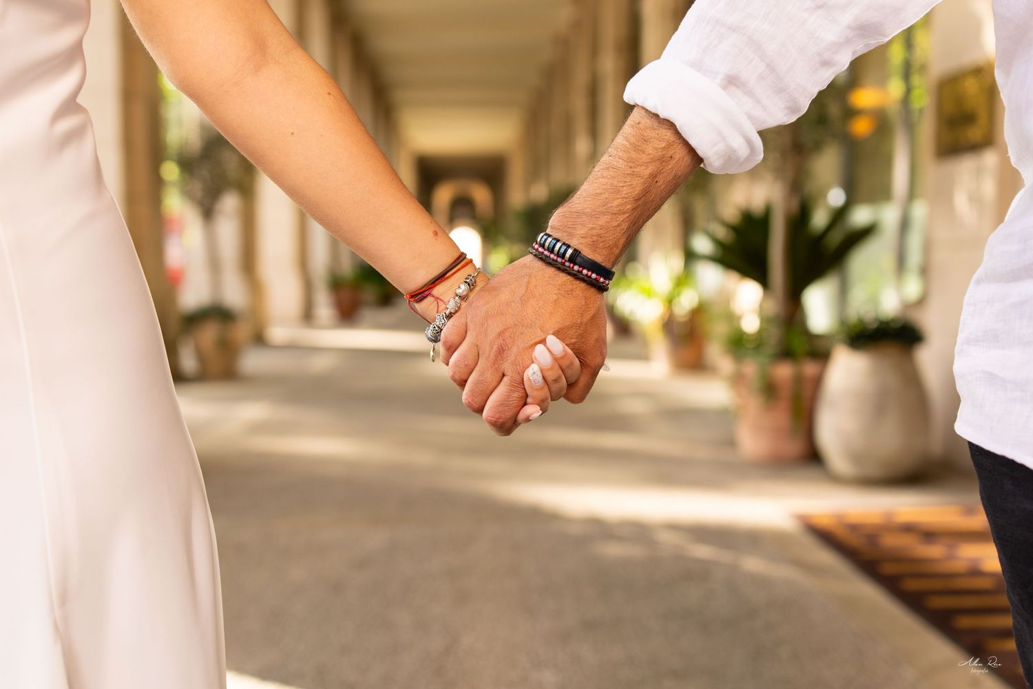 Close-up of couple holding hands in an arcade, showing matching bracelets and wedding ring.