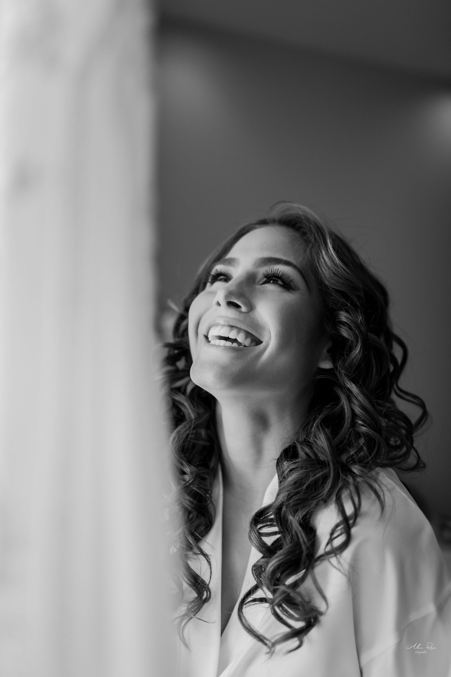 Black and white portrait of a radiant bride with curly hair laughing joyfully on her wedding day.