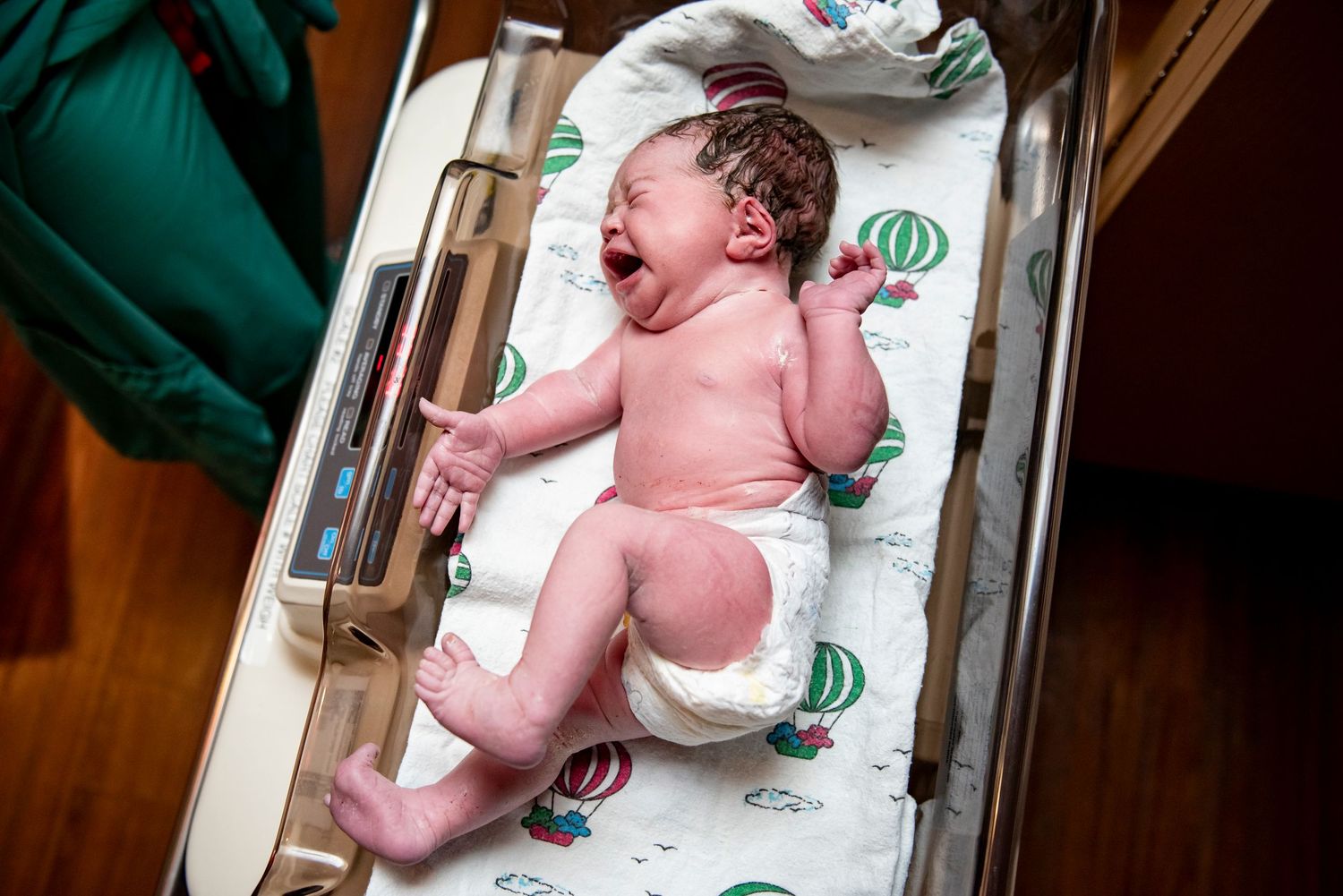 Newborn baby crying in hospital bassinet after birth, wearing diaper on patterned blanket.