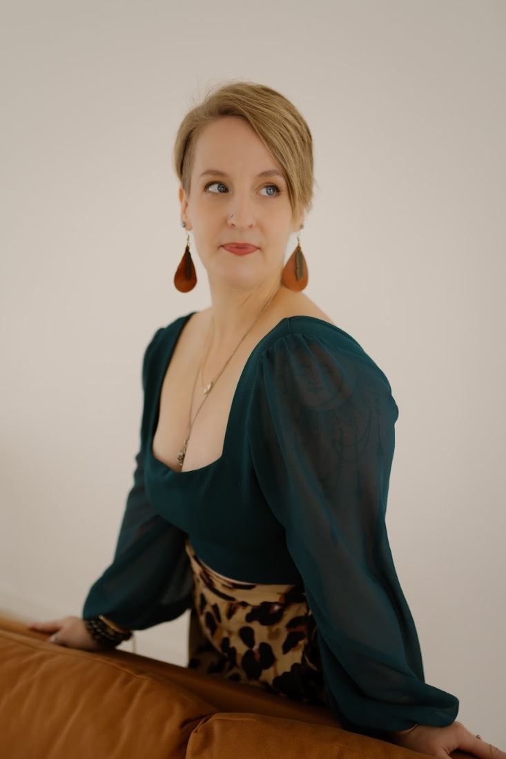 Woman in teal blouse and leopard skirt with brown teardrop earrings poses elegantly against a light background.