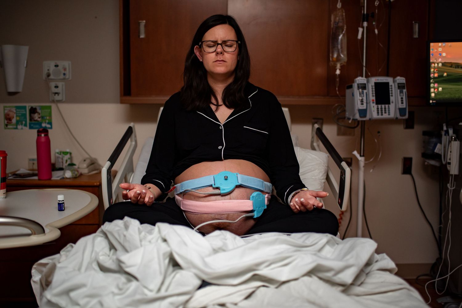 Pregnant woman meditating in hospital bed with fetal monitors attached during labor.