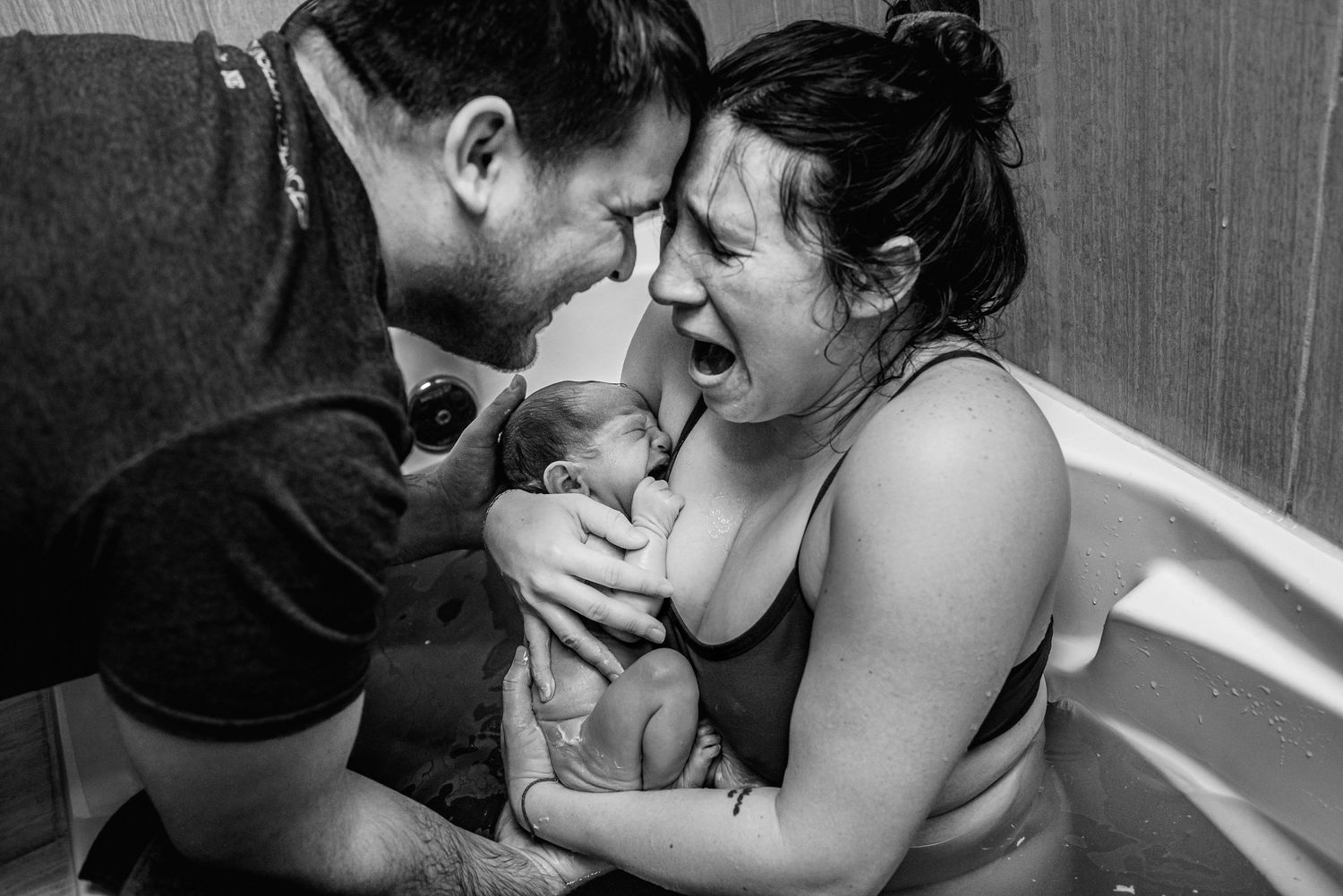Black and white image of couple sharing emotional moment with newborn in birth tub.