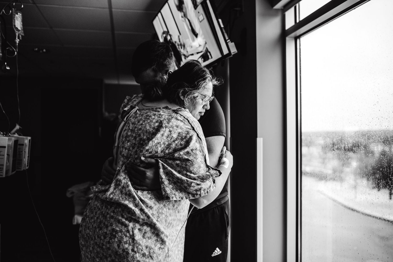 Black and white photo of pregnant woman being embraced near hospital window during labor.