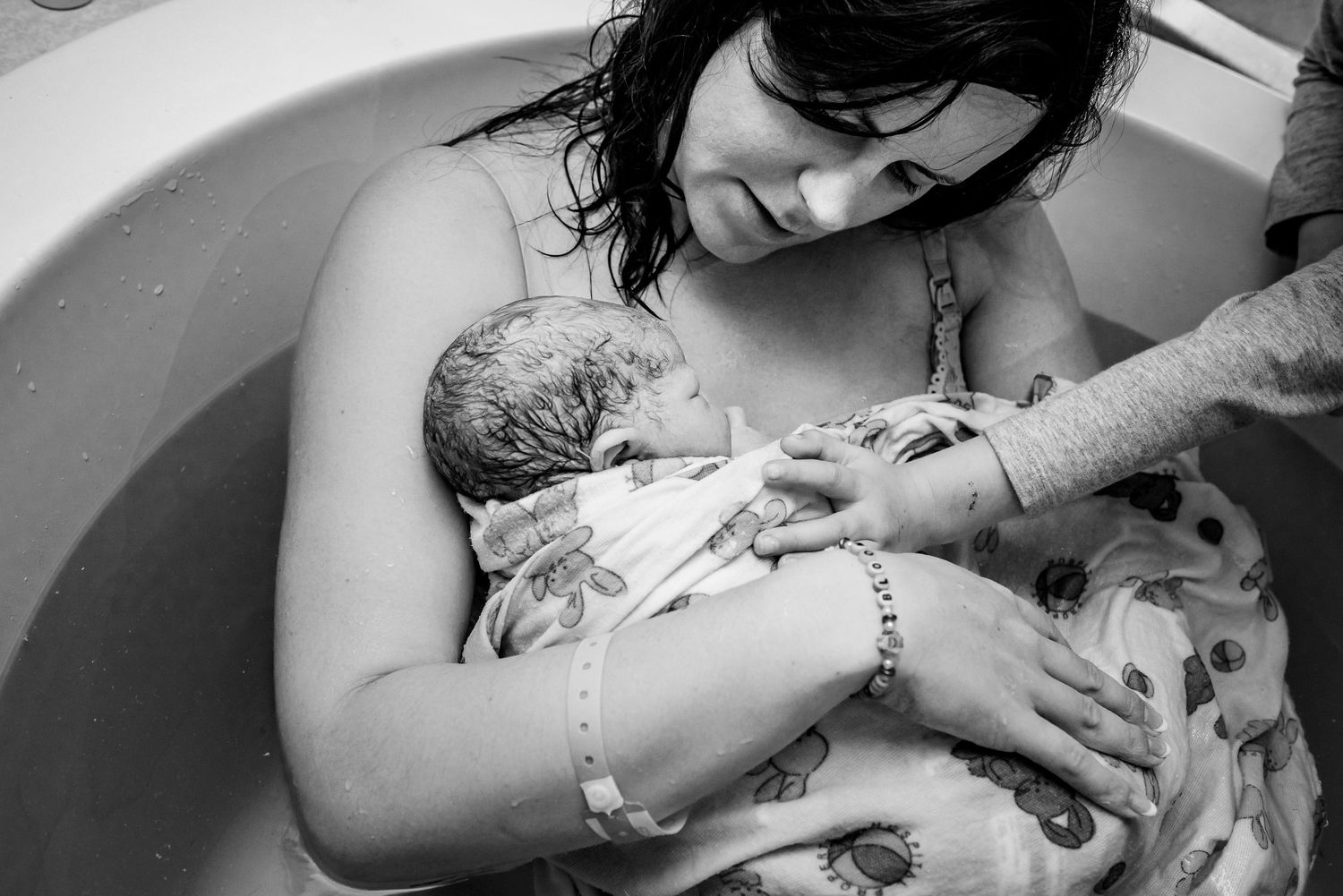 Black and white photo of tattooed mother holding newborn in hospital birthing tub.
