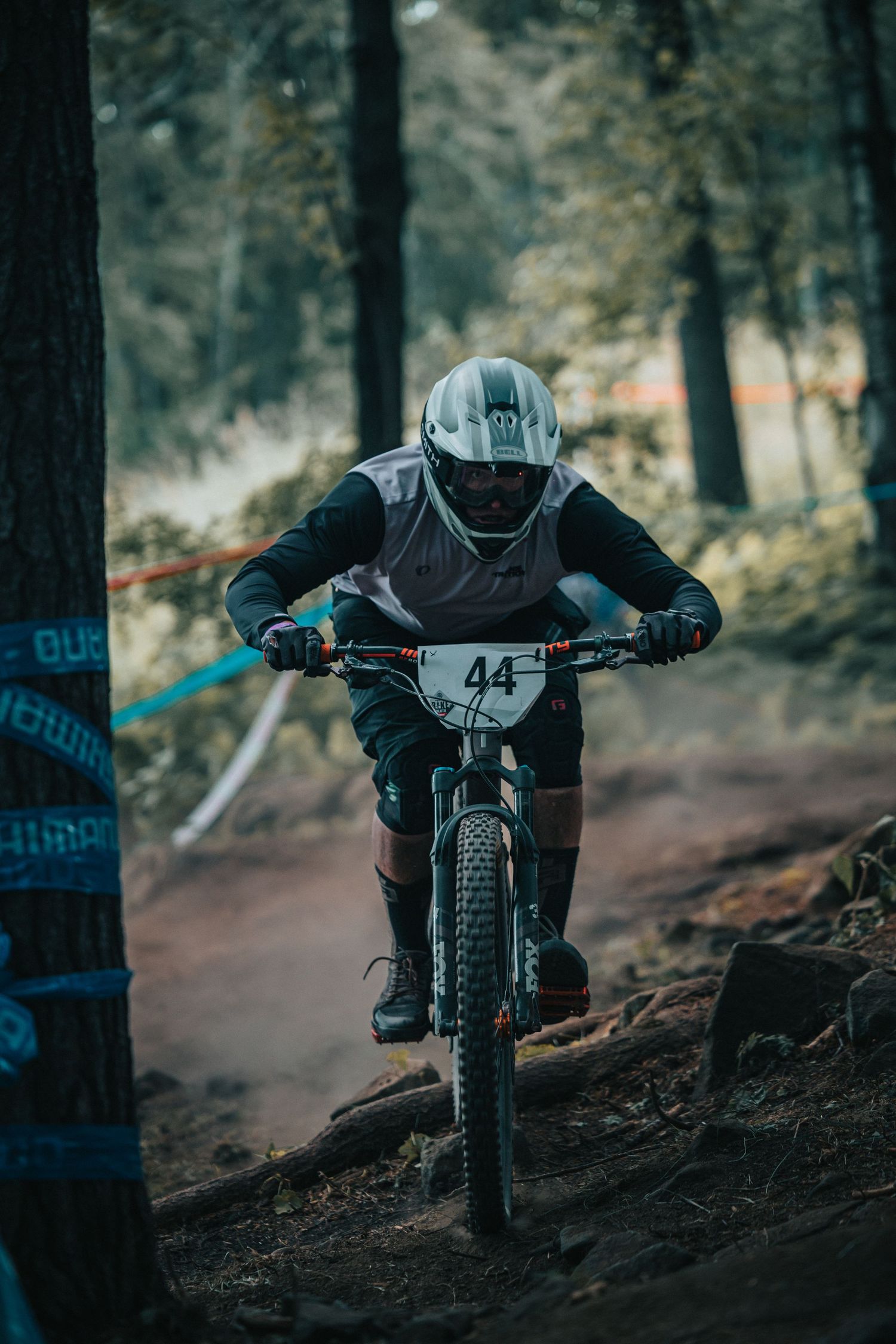 Mountain biker wearing number 44 racing downhill on dirt trail through pine forest.