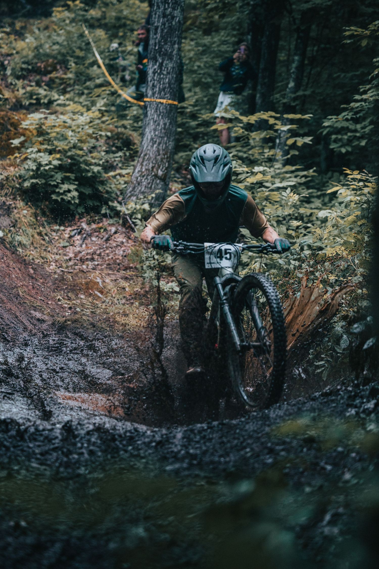 Mountain biker #45 rides through a muddy forest trail during a downhill enduro race competition.